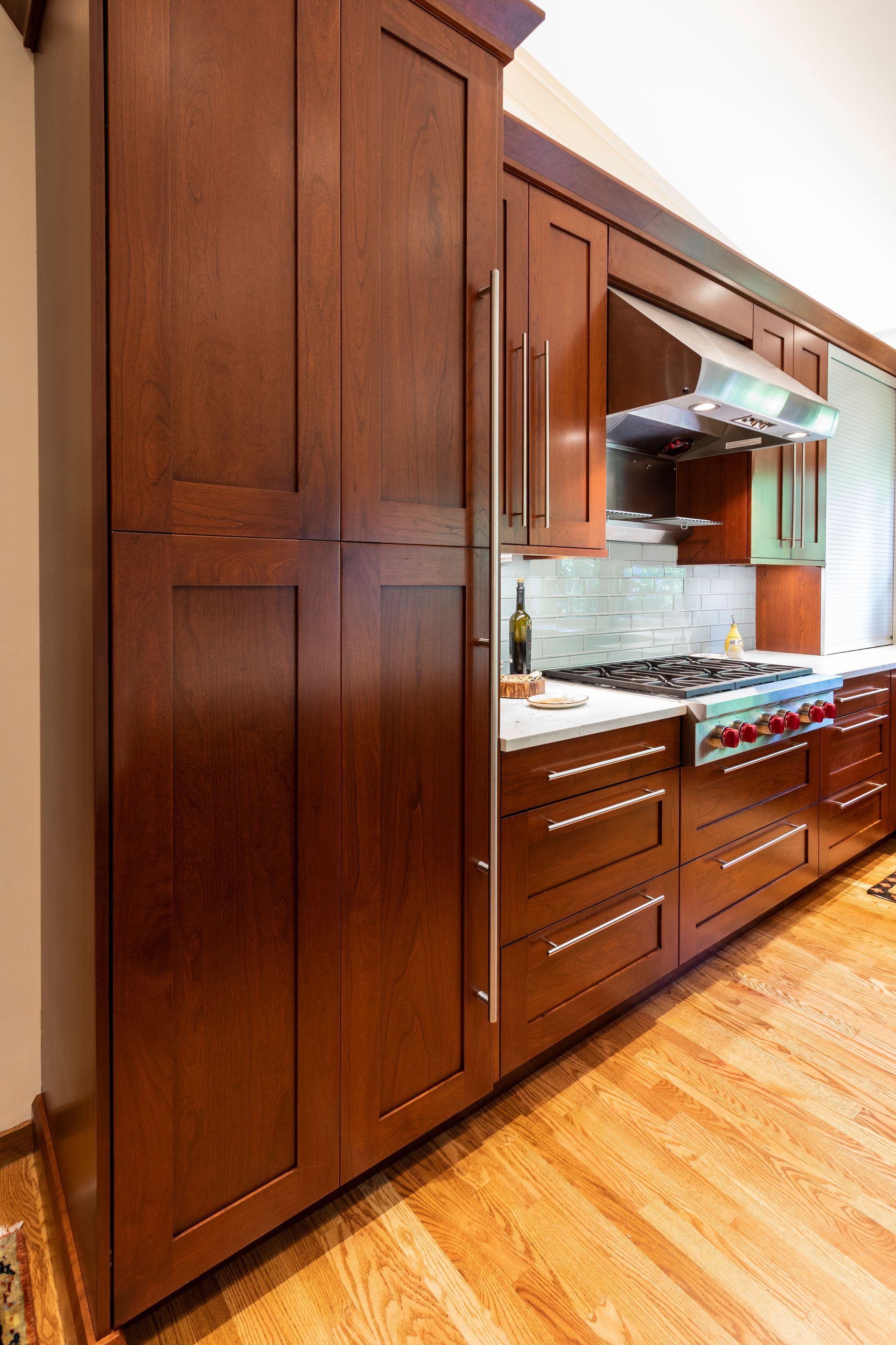 Tall cherry wood kitchen cabinets with stainless steel hardware, next to a stove.