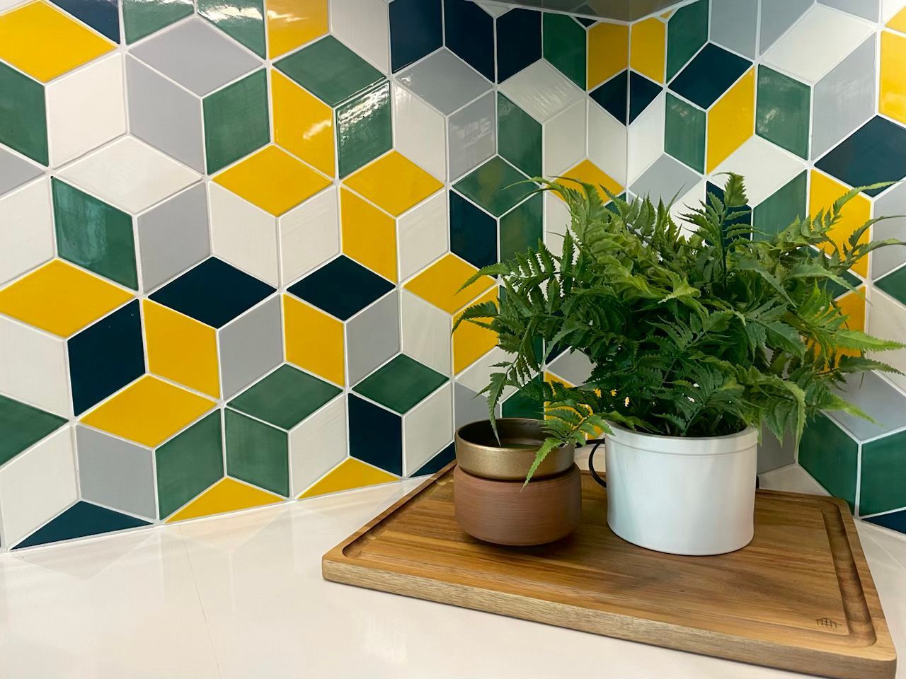 Colorful geometric tile backsplash with potted ferns on a wooden tray.