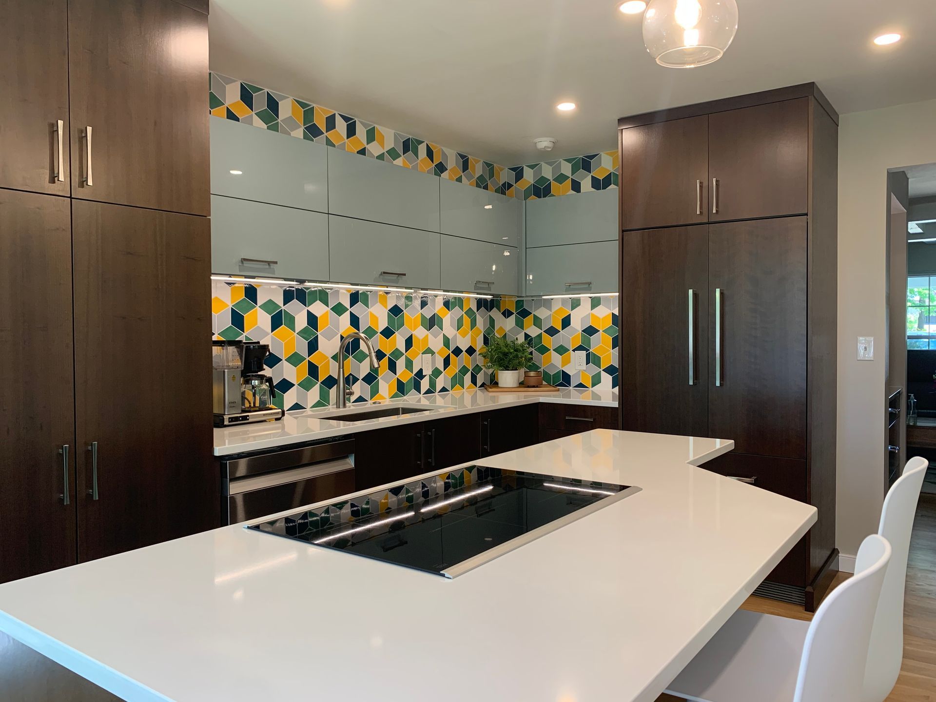 Modern kitchen with dark cabinetry, white countertops, and geometric tile backsplash.