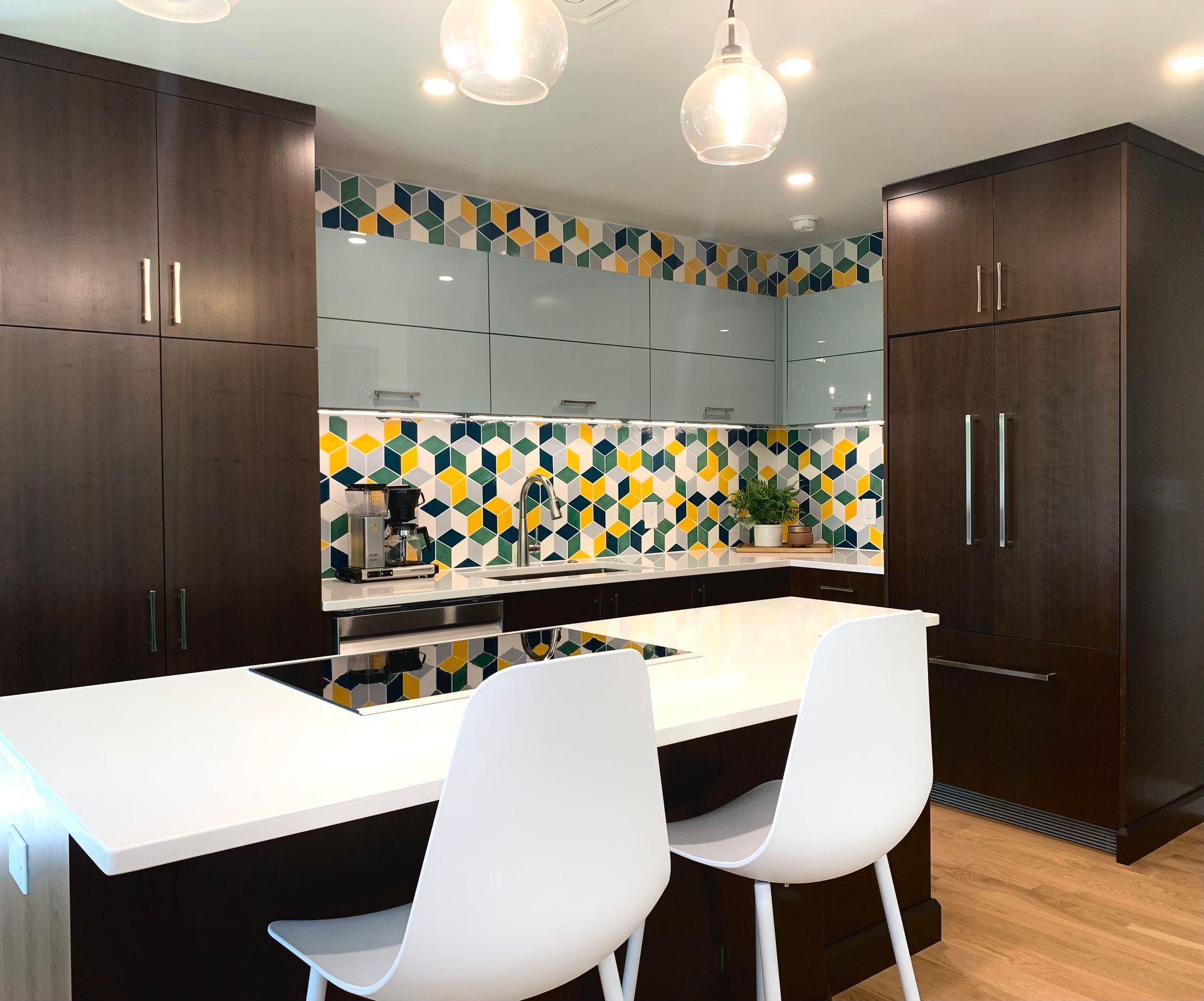 Modern kitchen with dark cabinetry, white countertops, and colorful backsplash. Two white chairs at island.