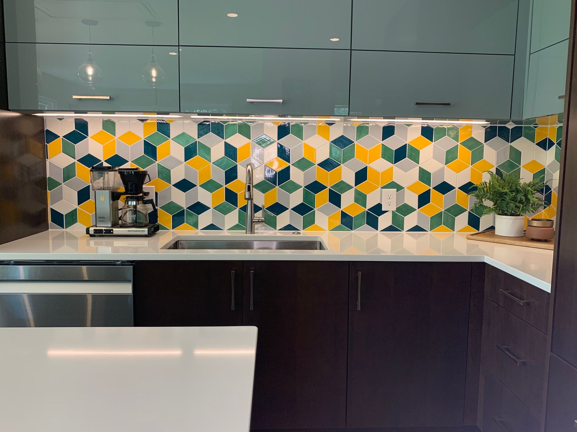 Kitchen with geometric tile backsplash, dark cabinets, and stainless steel appliances.