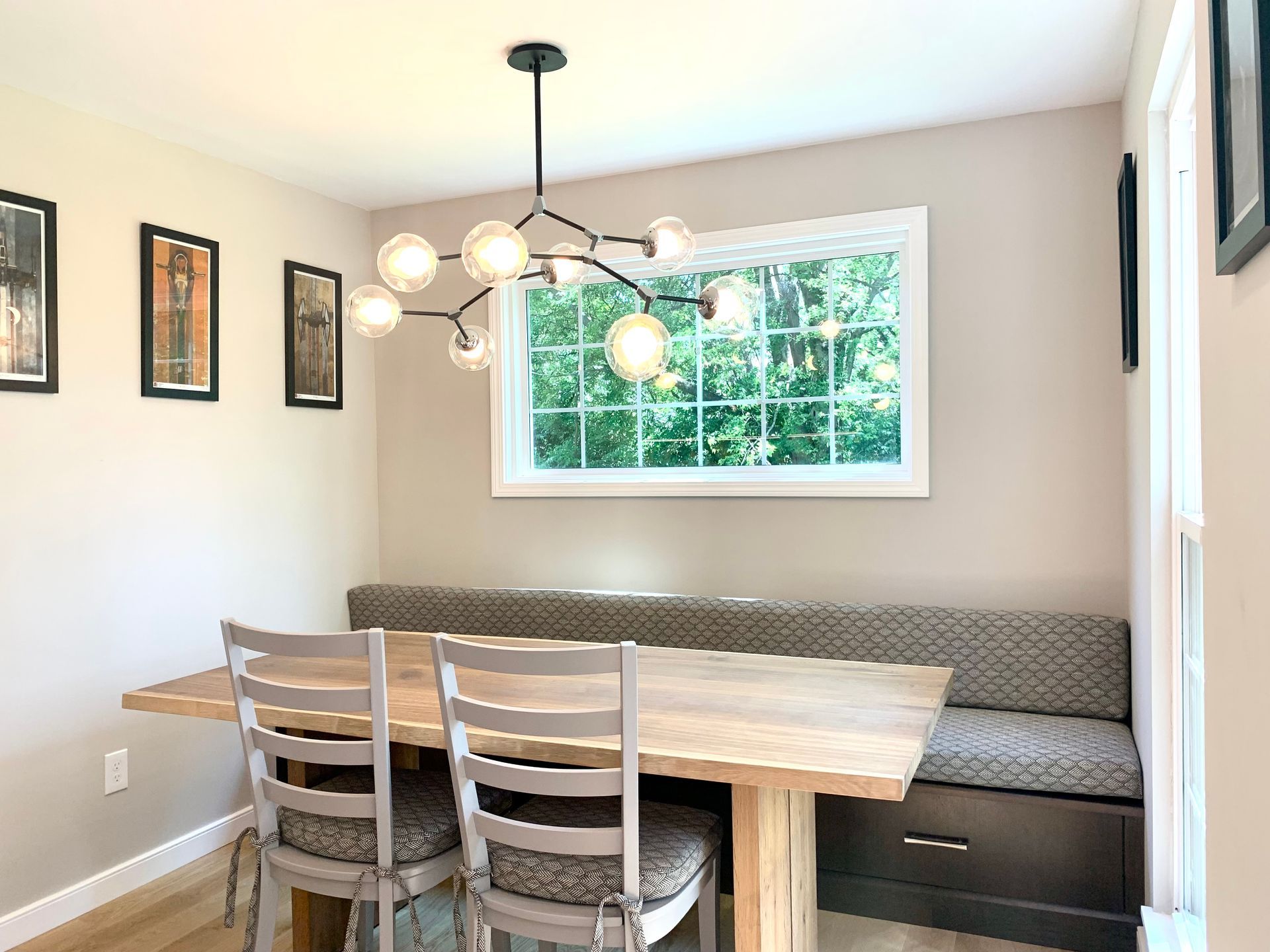 Dining nook with wooden table, built-in bench, two chairs, and a window with a chandelier.
