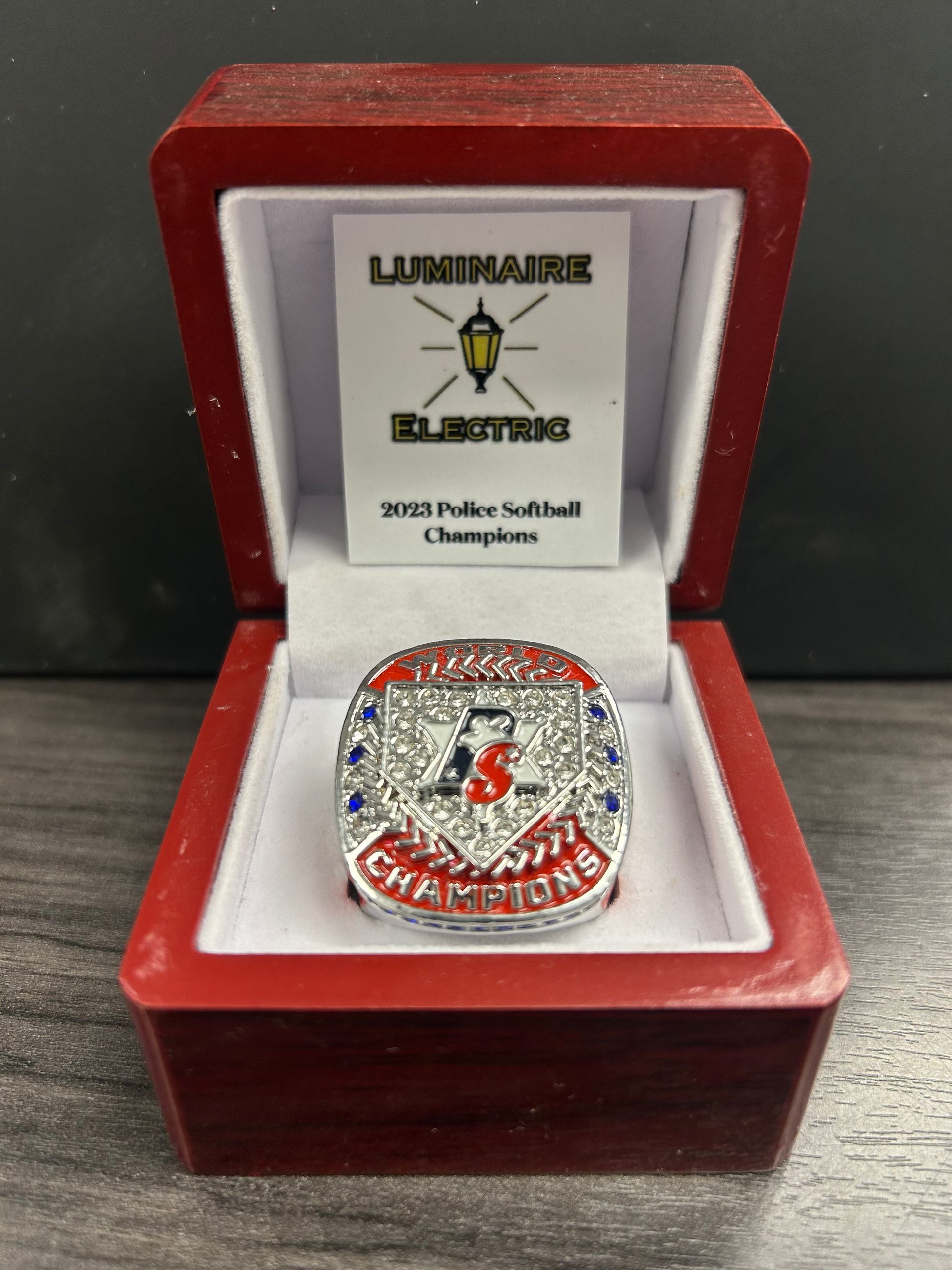 Red jewelry box holding a silver ring with red stones and an engraved softball champion plaque