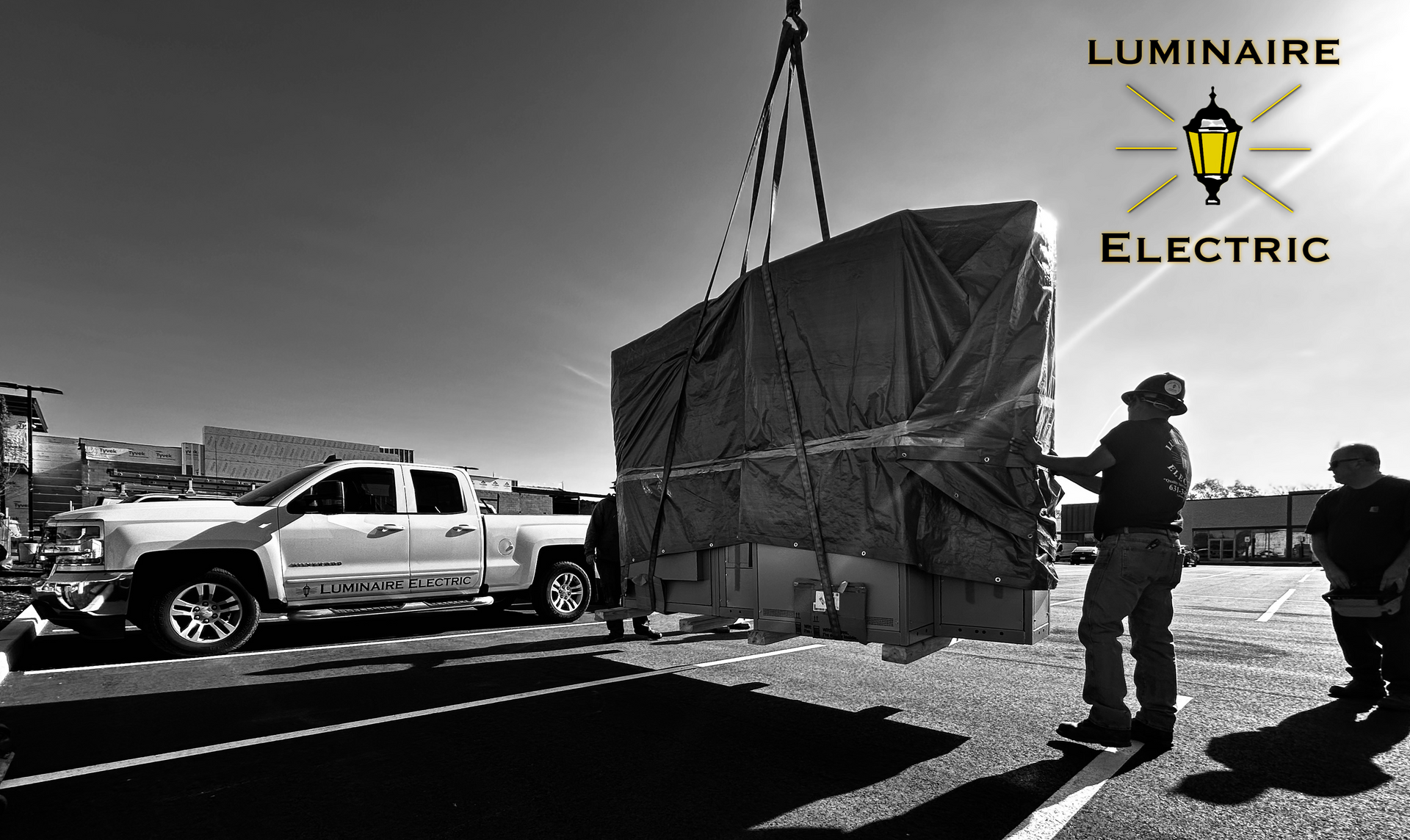A truck is being lifted by a crane with the words Luminaire Electric in the background