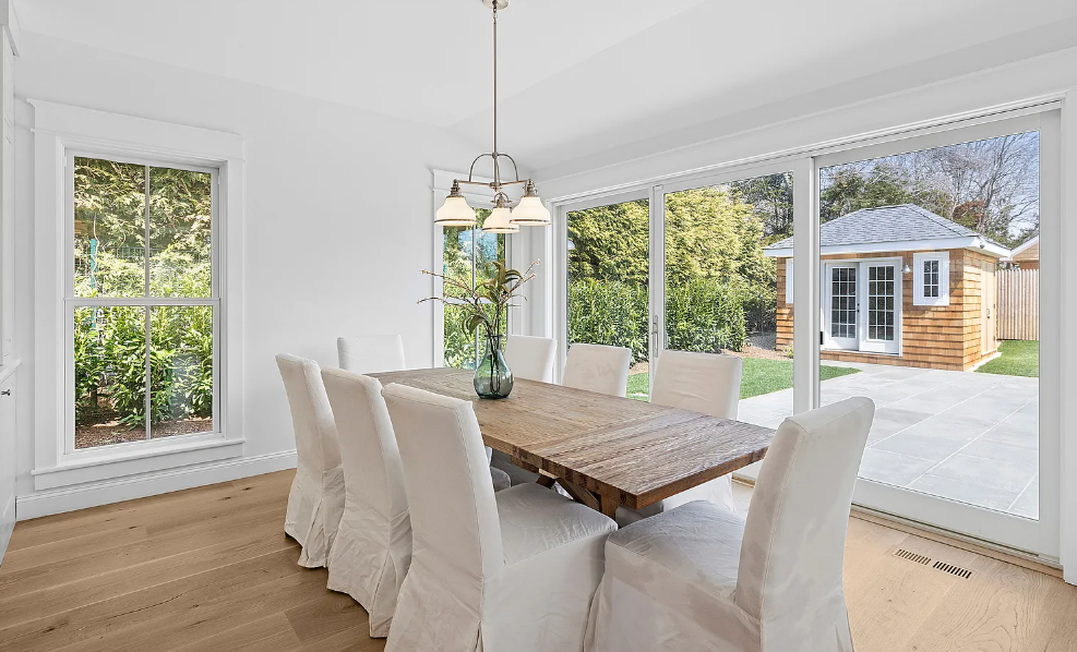 A dining room with a wooden table and white chairs.