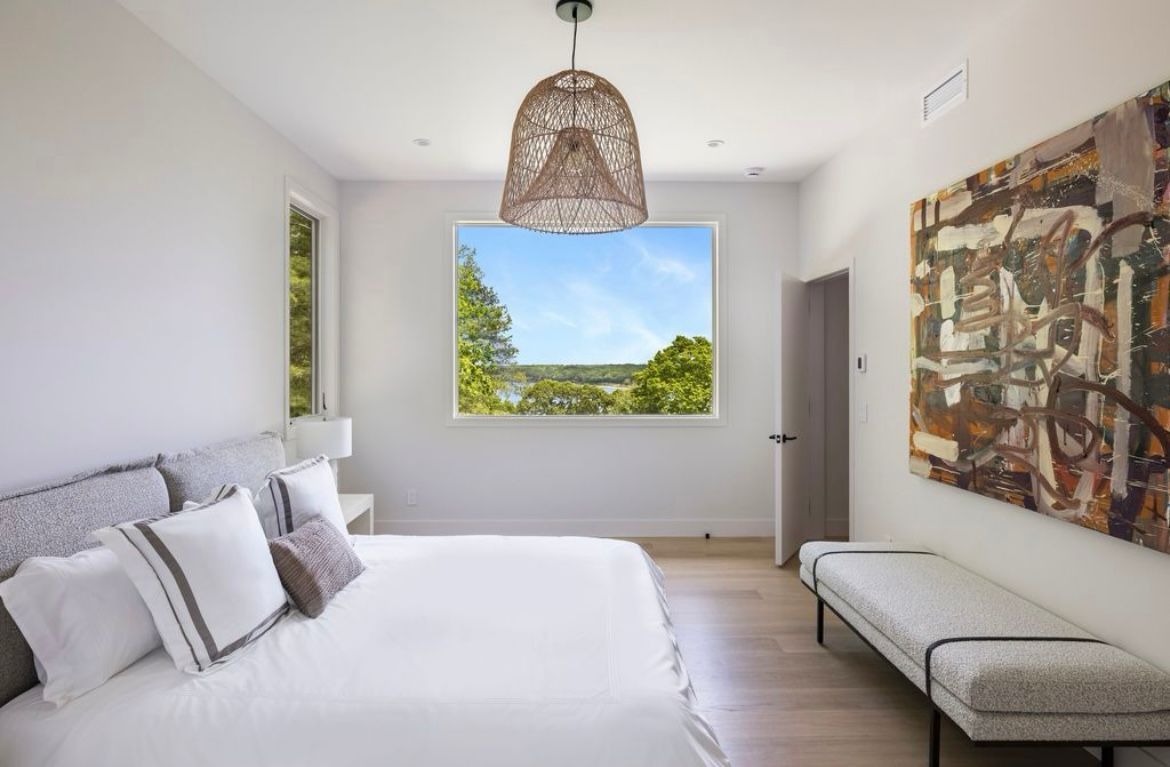 A bedroom with a large bed, a bench, a window and a painting on the wall