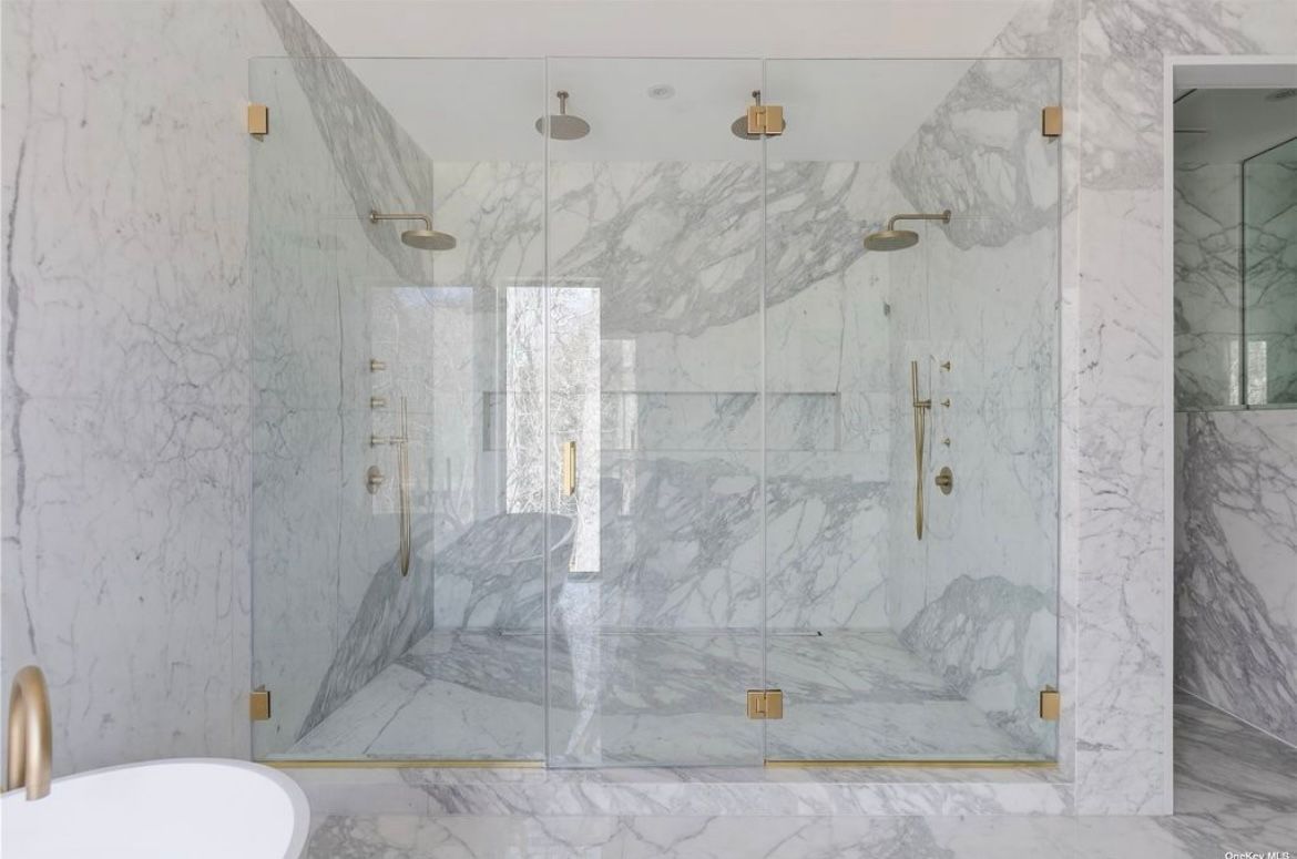 A bathroom with marble walls and a walk in shower with a glass door