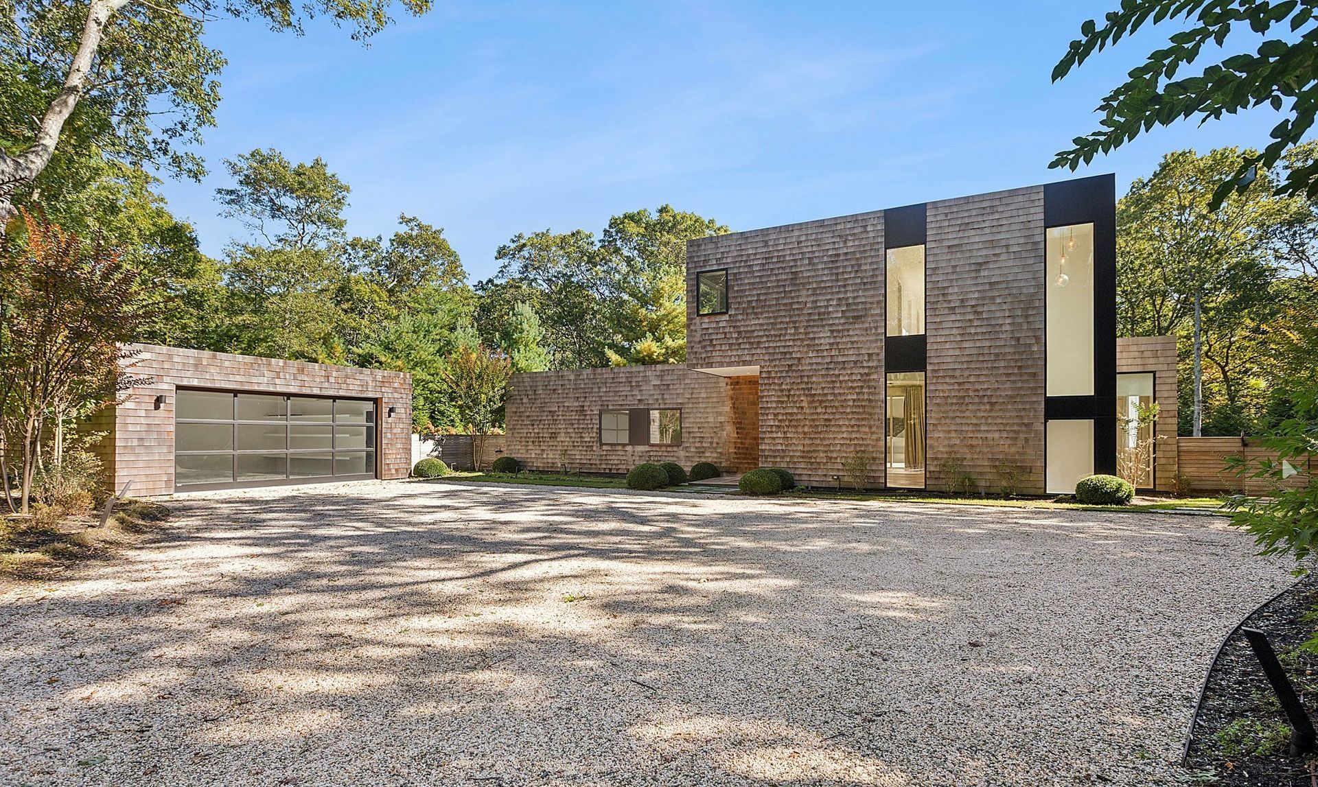 Modern two-story brick house with a detached garage, wide gravel driveway, and trees around it