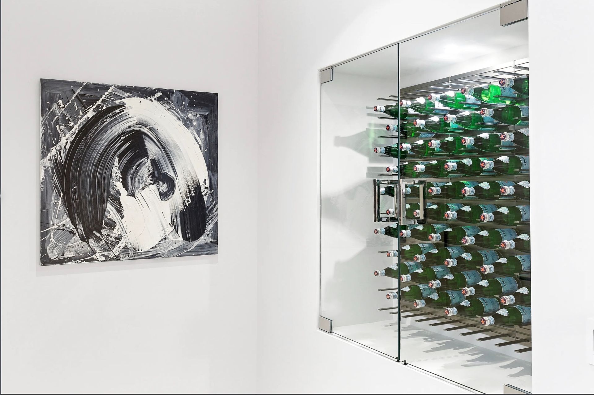 Art gallery wall with abstract black-and-white painting and glass display of green bottles