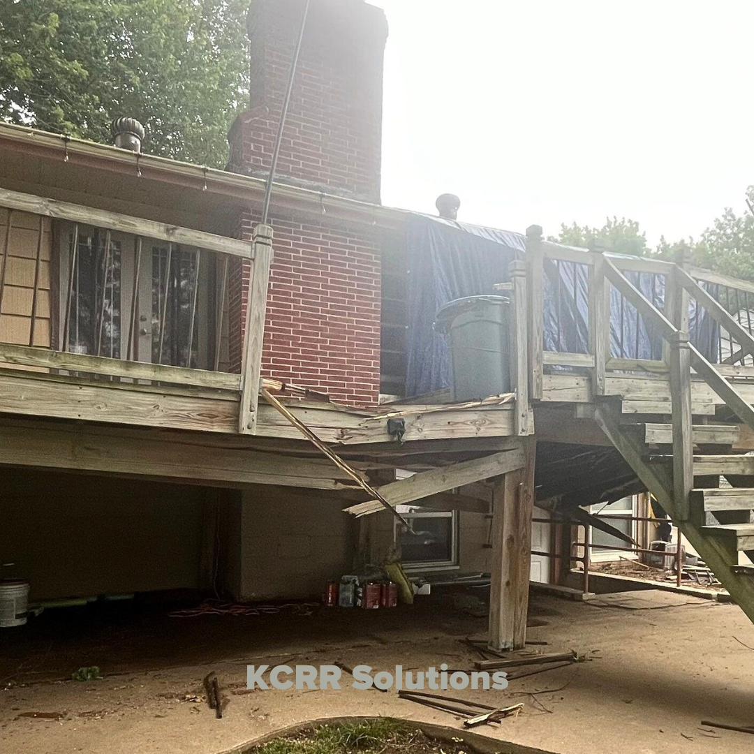 Photo of a storm-damaged deck with broken railings and sagging support beams. A tarp covers part of the roof to prevent further damage, while the deck stairs and lower structure show signs of failure from the storm's impact.
