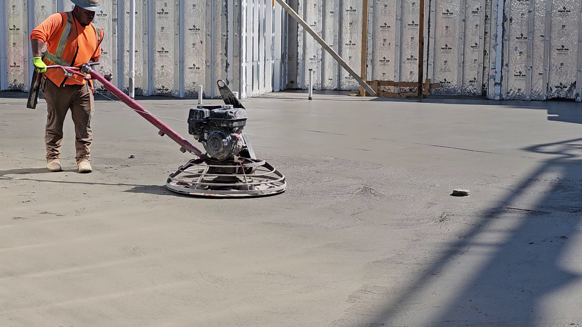Construction worker operating a concrete power trowel on a cement floor. Outdoors, sunny.