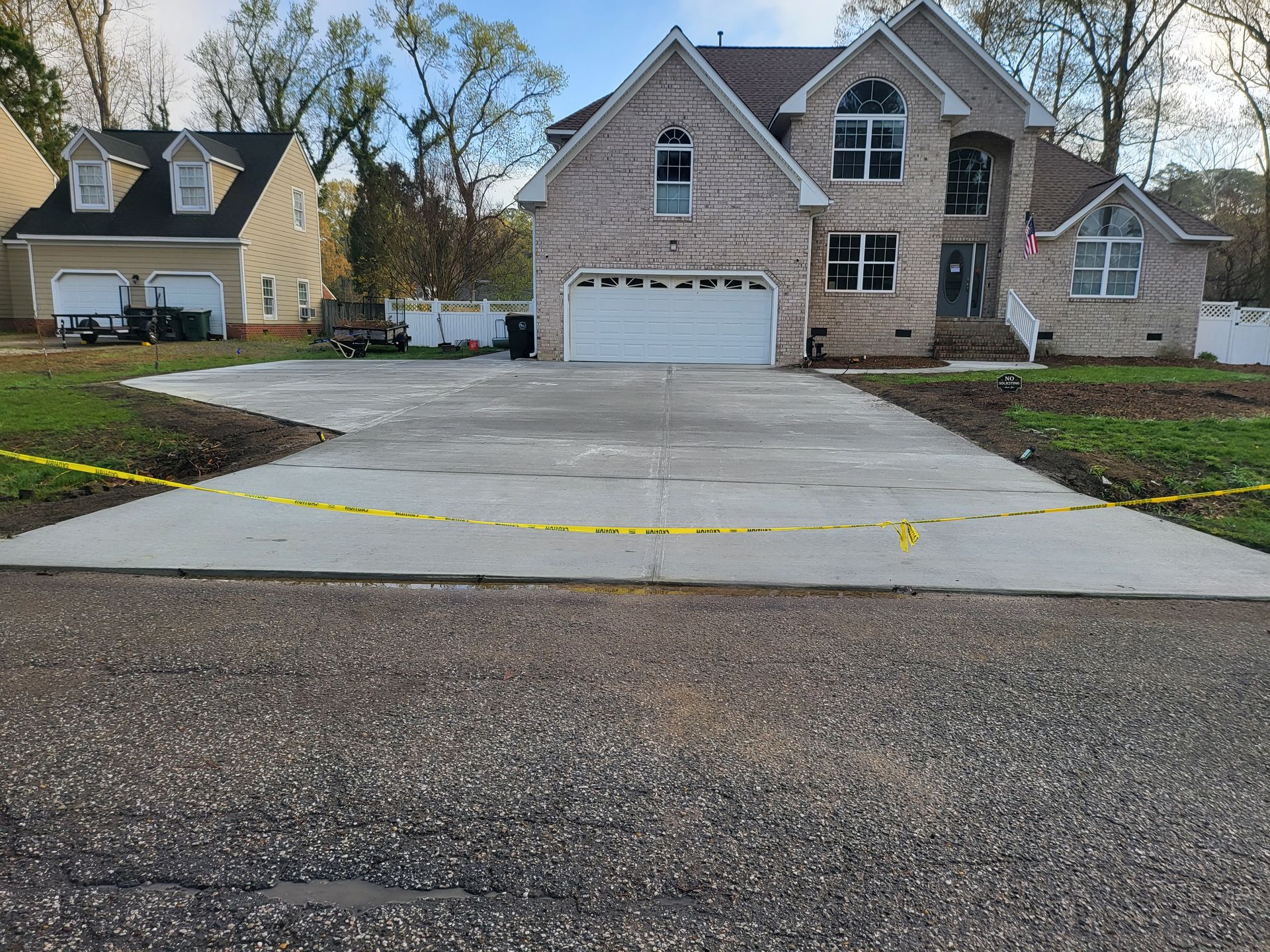 Newly poured concrete driveway in front of a two-story brick house with a white garage door.