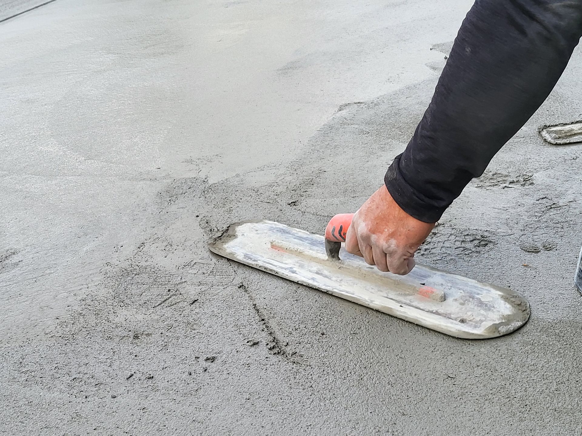 Person smoothing wet concrete with a trowel, outdoors.