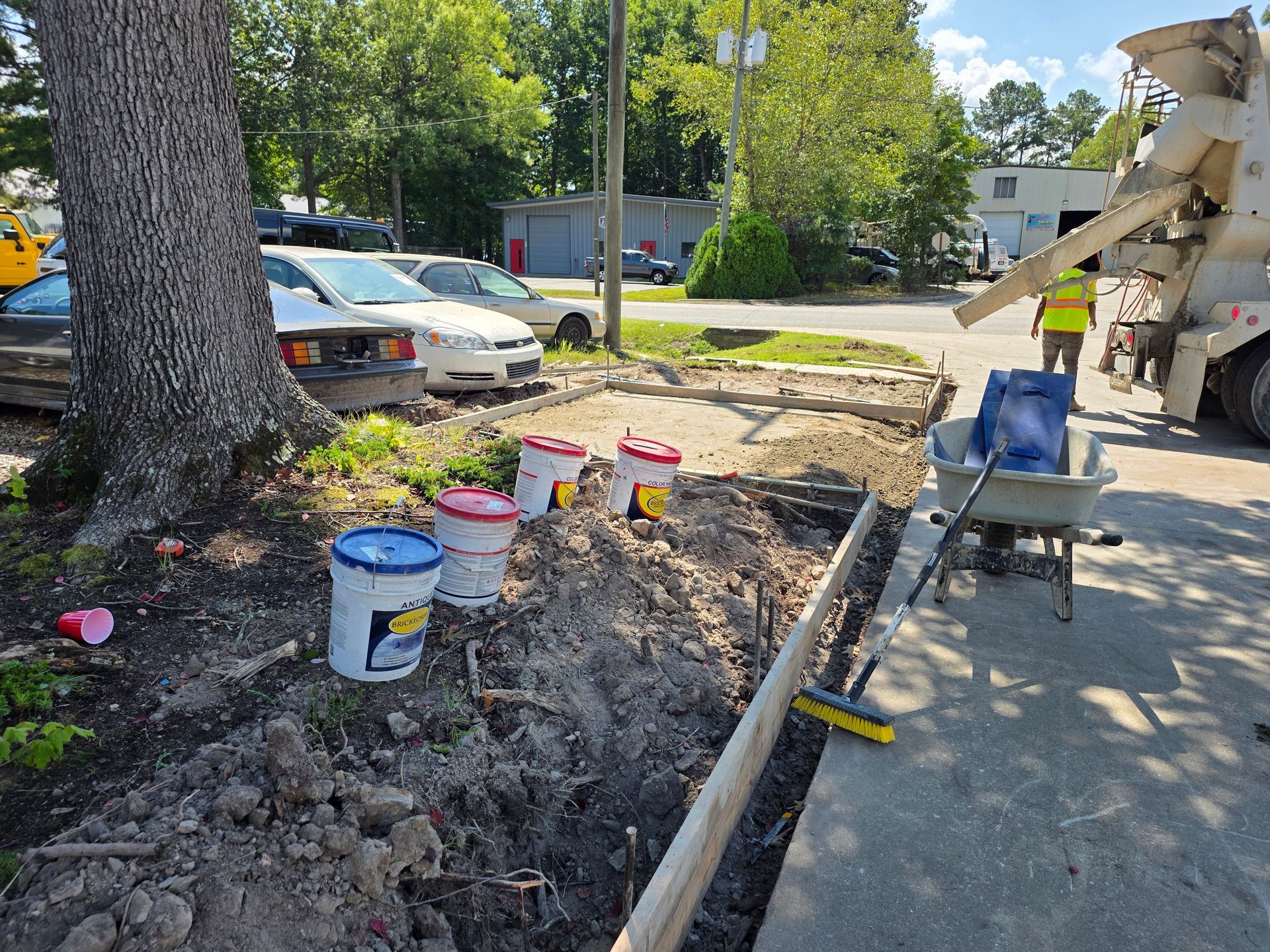 Construction site: Cement being poured; buckets, wheelbarrow, and concrete forms are visible.