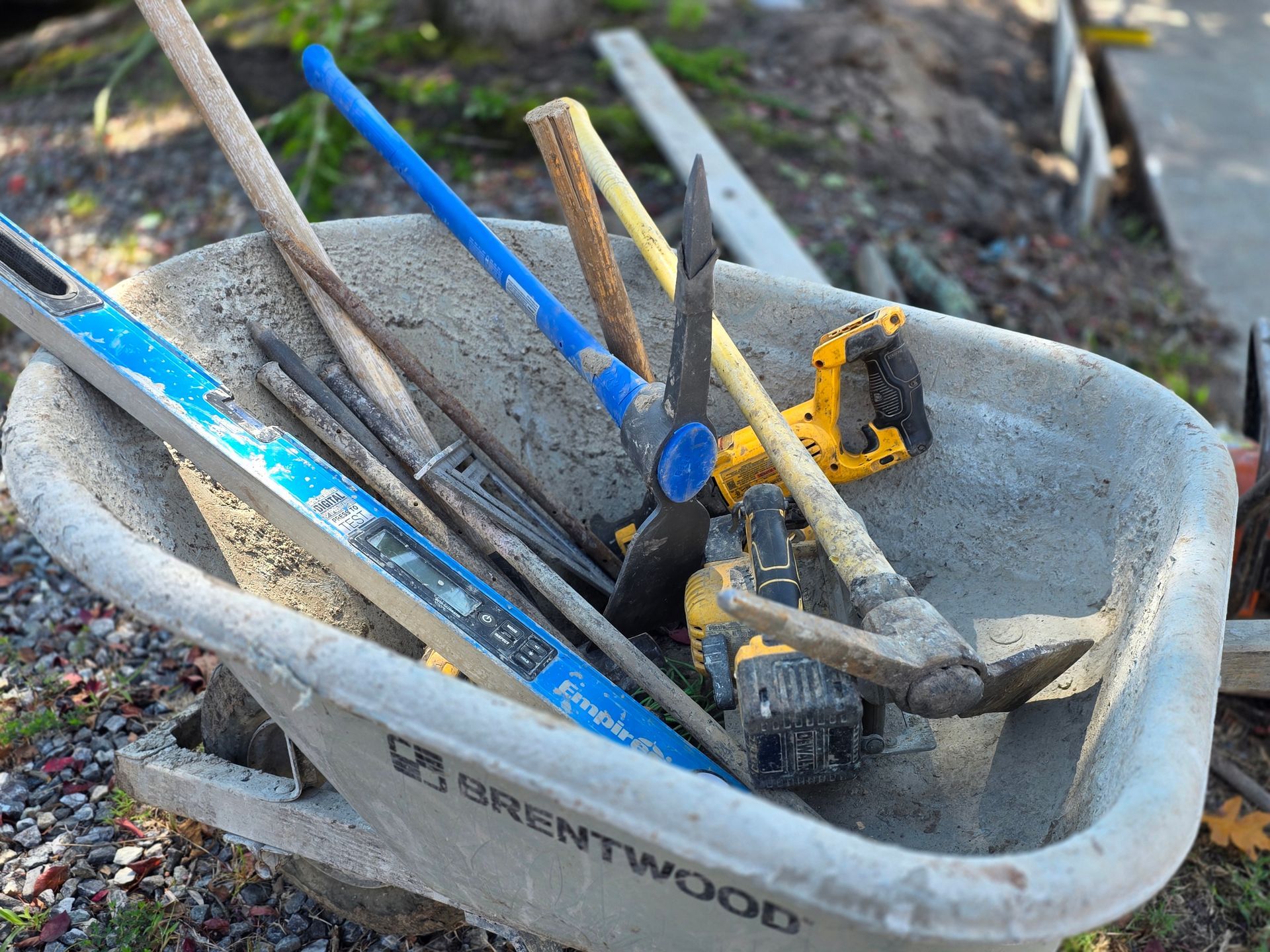 Wheelbarrow filled with construction tools: level, pickaxe, saw, and other hand tools.