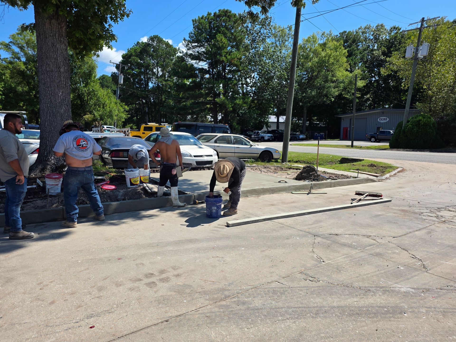 Construction workers pouring concrete at a curb, sunny day.
