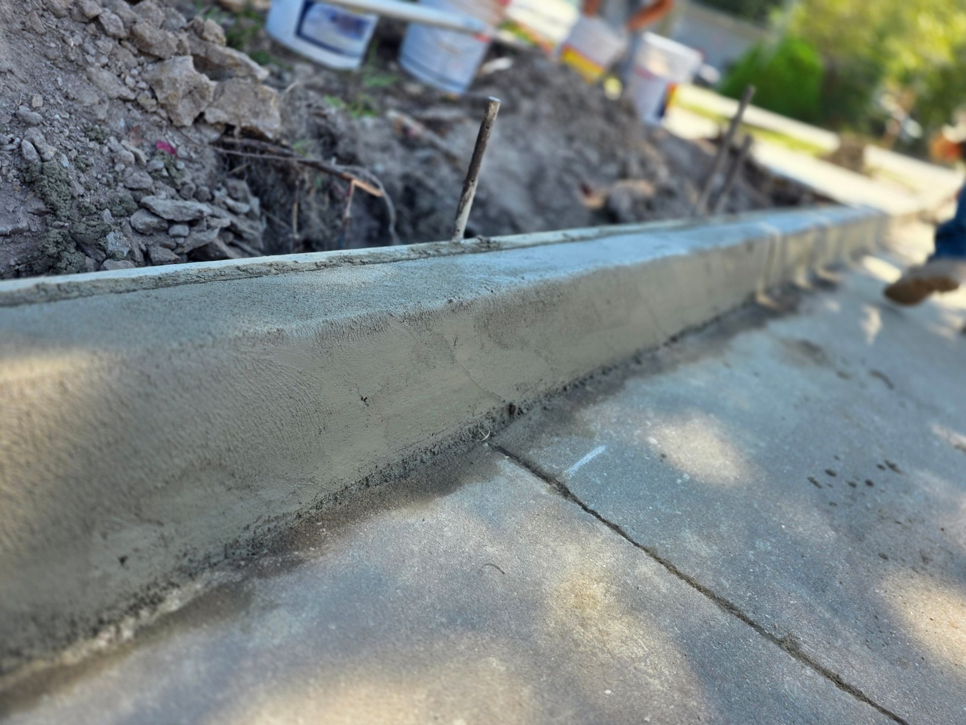 Freshly poured concrete curb next to existing concrete sidewalk; construction site.