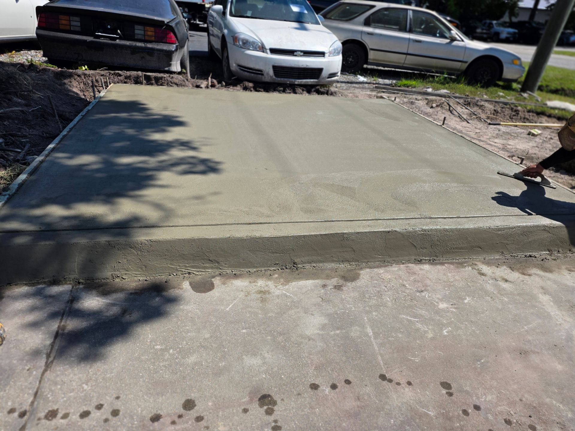 Freshly poured concrete driveway section with cars parked behind.
