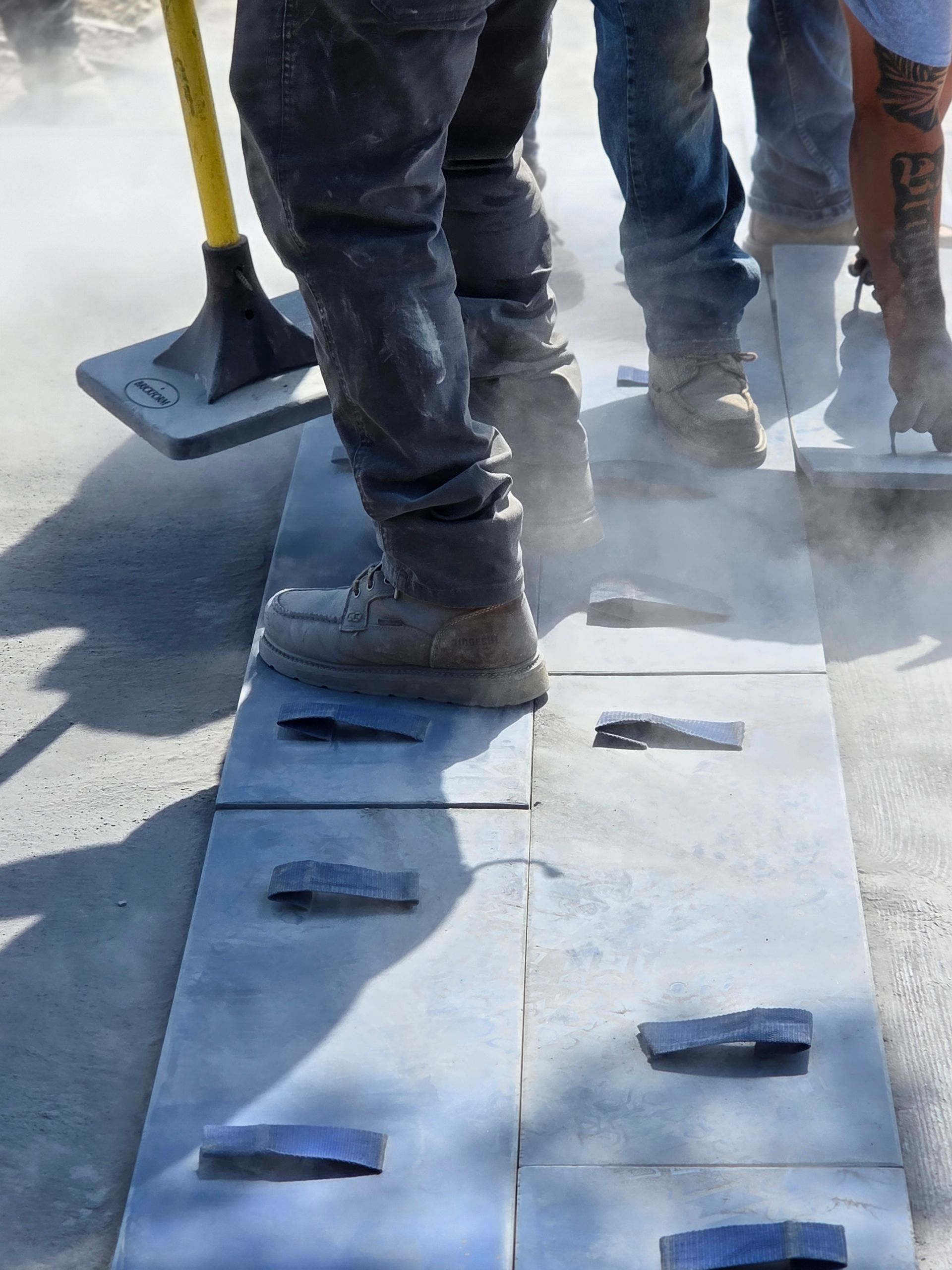 Construction workers standing on gray stepping stones, using tools on a dusty worksite.