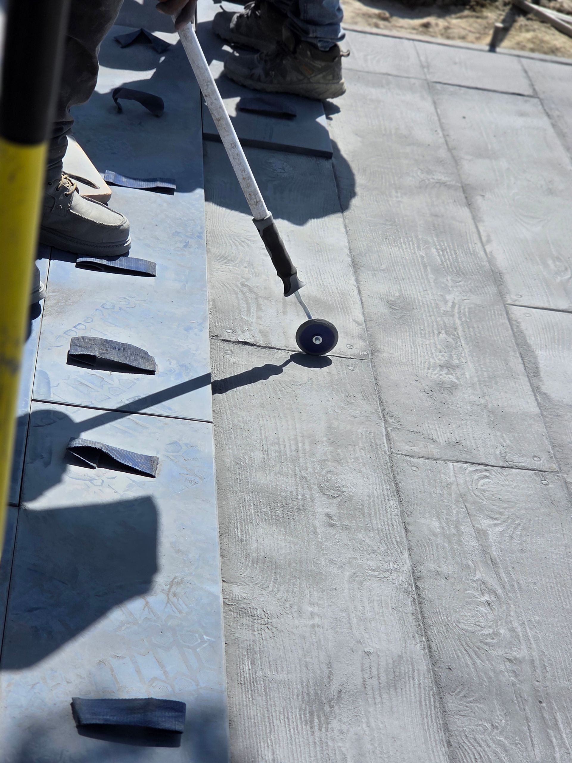 Person using a white cane, testing a tactile paving surface. Gray slabs with dark insets. Outdoor setting.