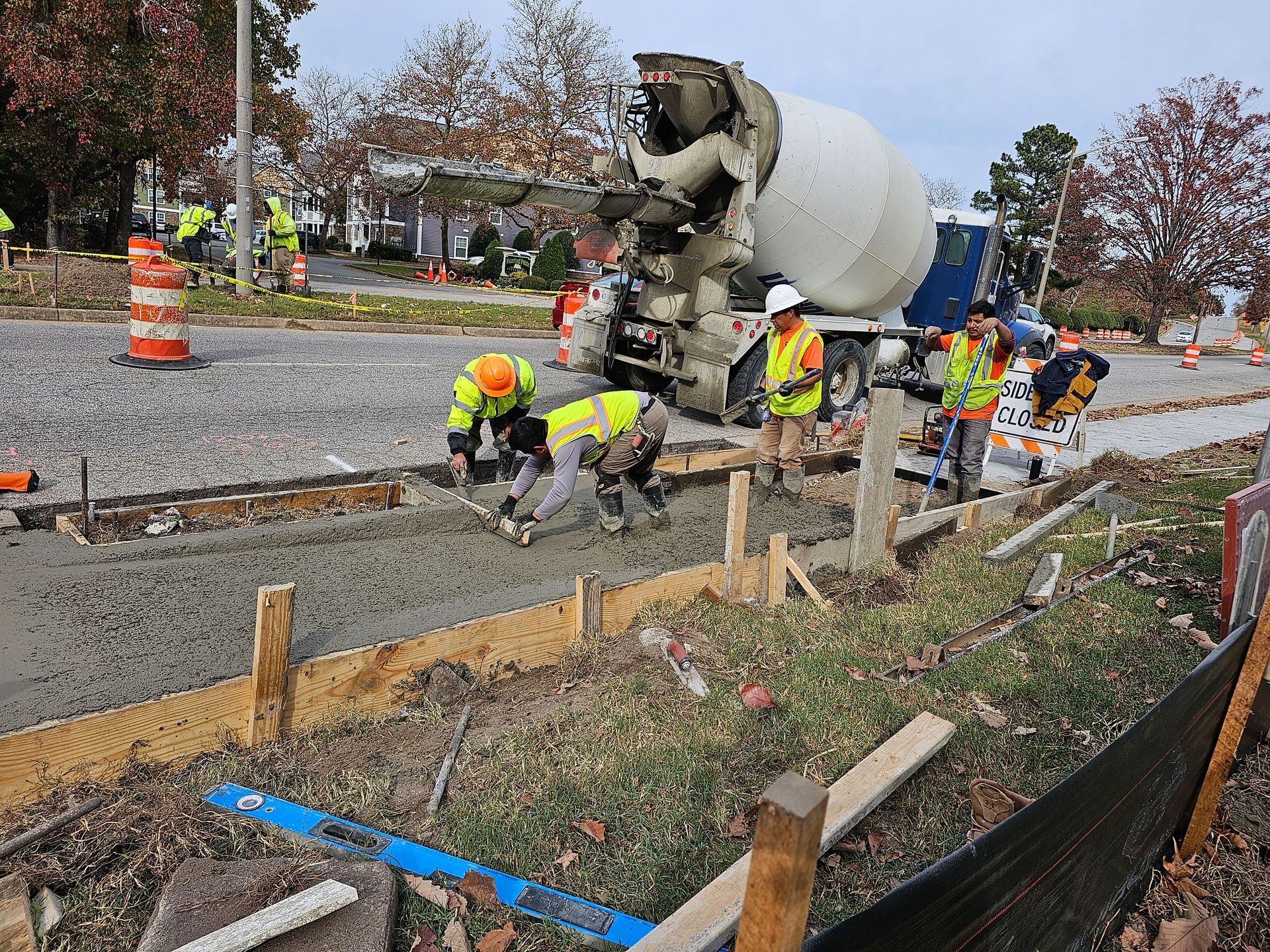 Construction workers pouring concrete from a truck into forms along a road.