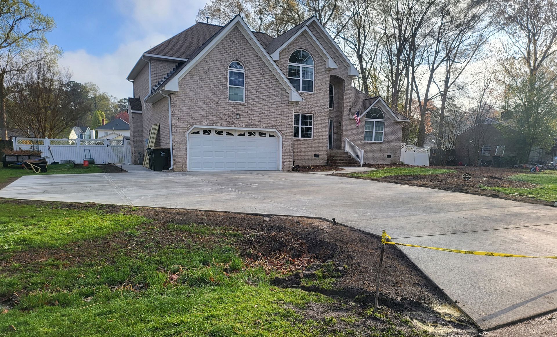 Brick house with gray driveway. Green lawn in the foreground and trees in the background under a cloudy sky.