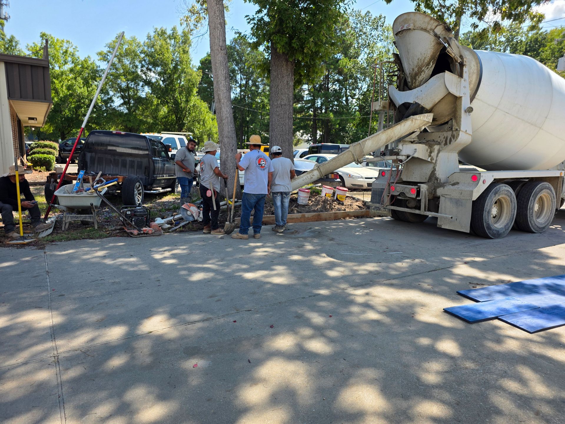 Concrete truck pouring concrete; workers in hard hats near a building; trees in background.