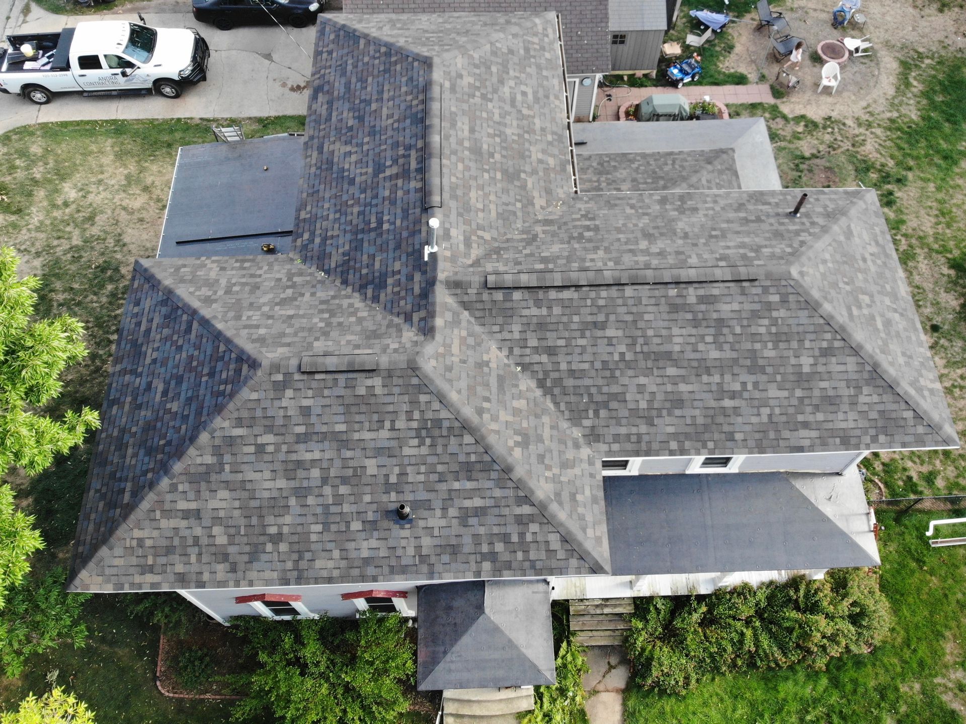 Overhead view of a house with a gray shingle roof. The house is surrounded by greenery and has several levels.