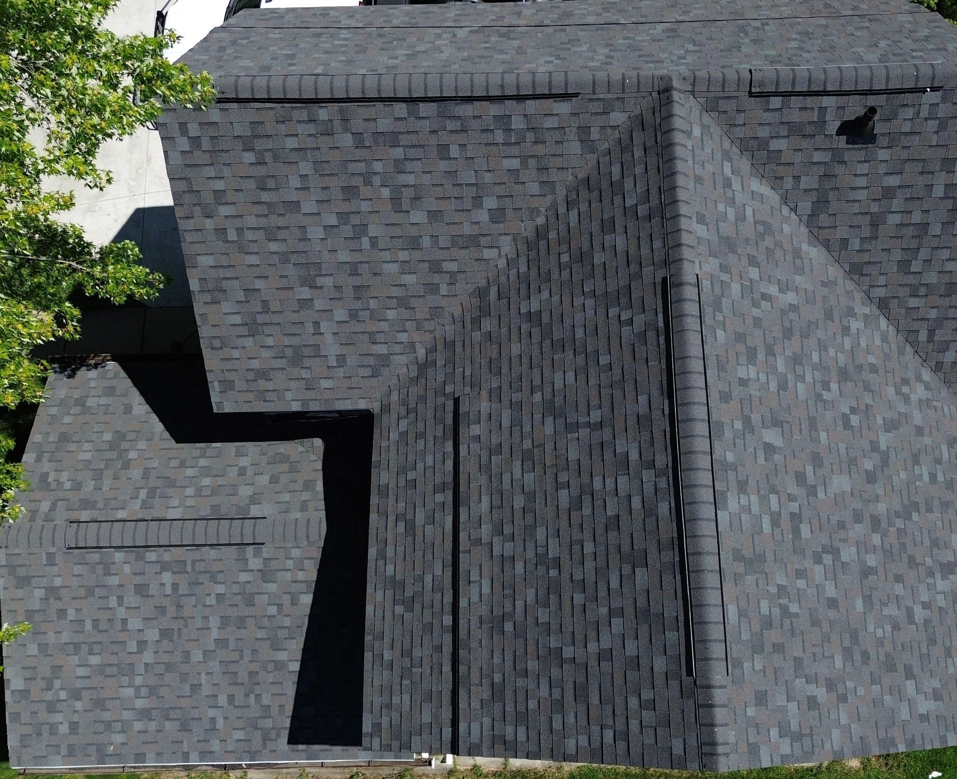 Dark gray shingled roof with geometric angles, visible from above. Sunlight casts shadows on the intersecting planes.