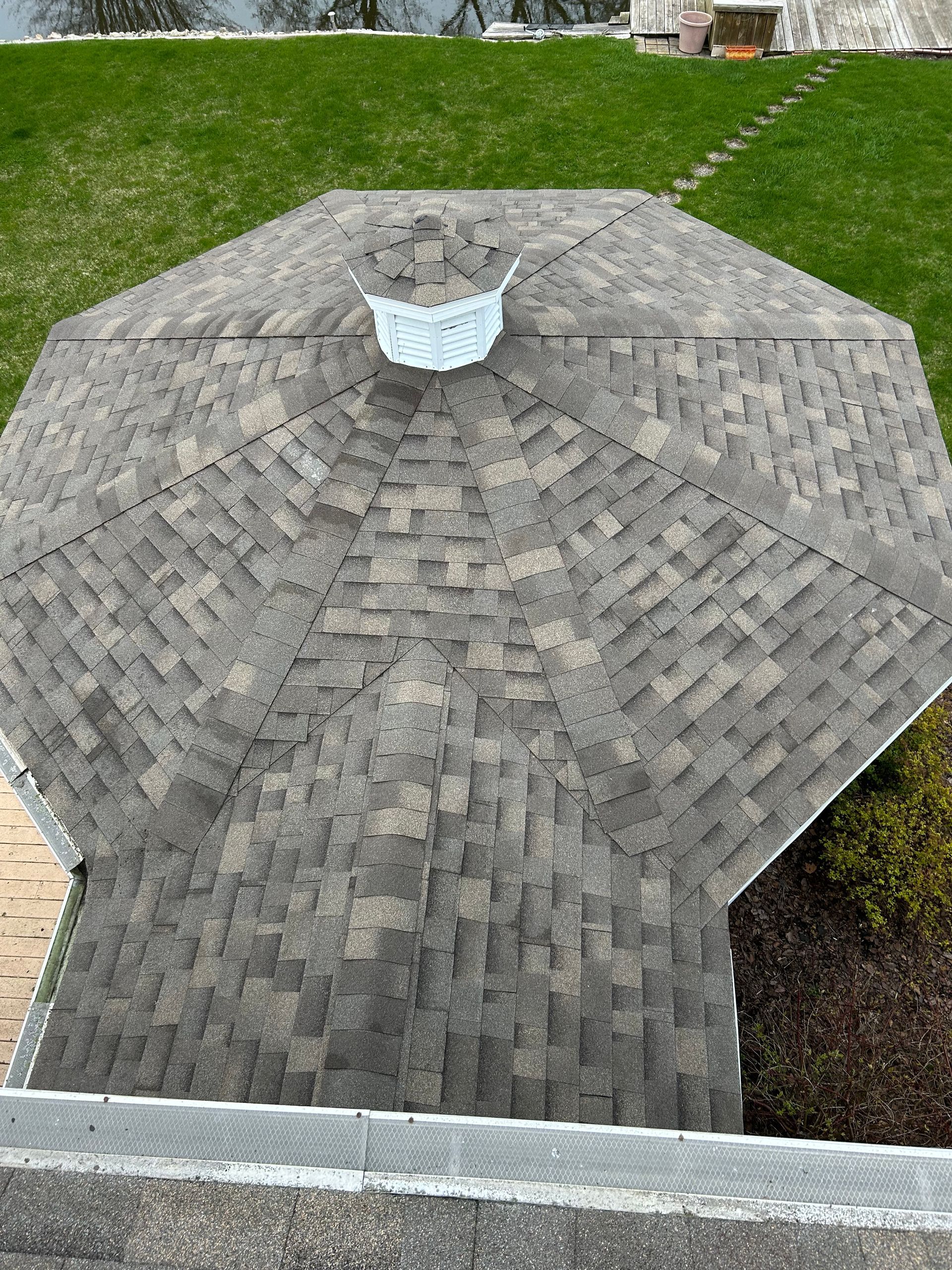 Octagonal roof with weathered asphalt shingles, light green grass surrounds it.