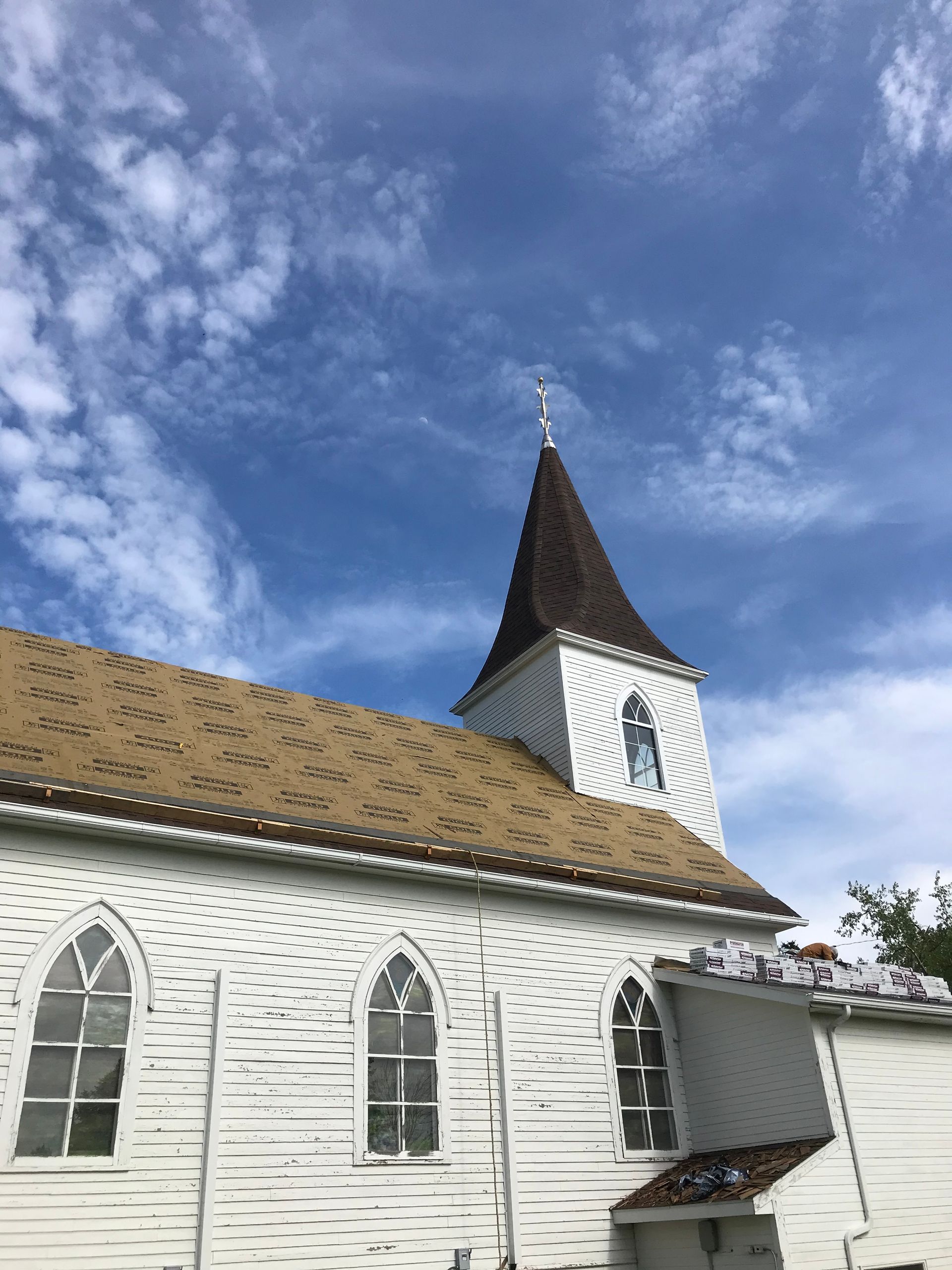 White church with brown roof and steeple against a blue sky with wispy clouds.