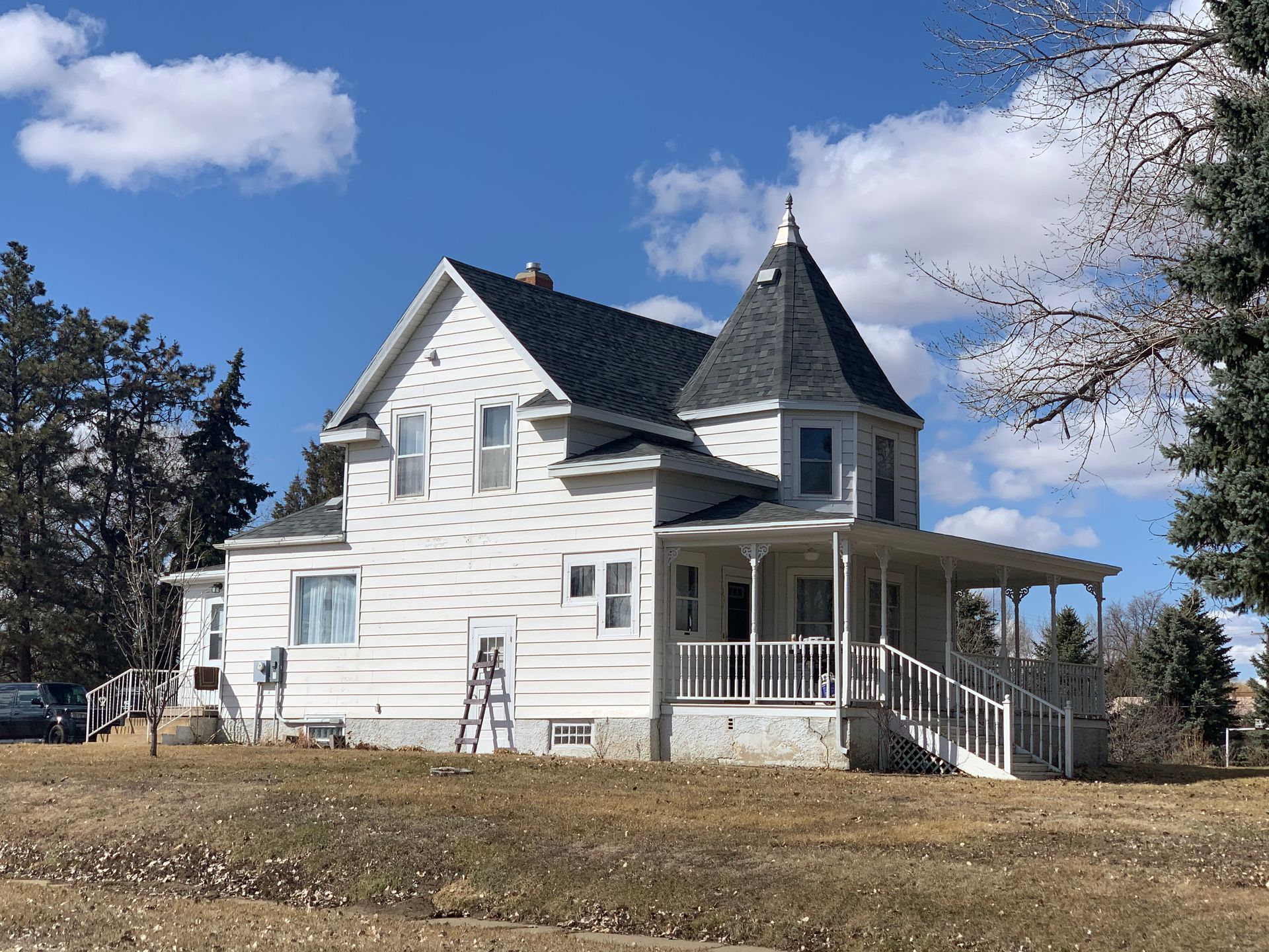 White Victorian house with a turret and porch under a blue sky.