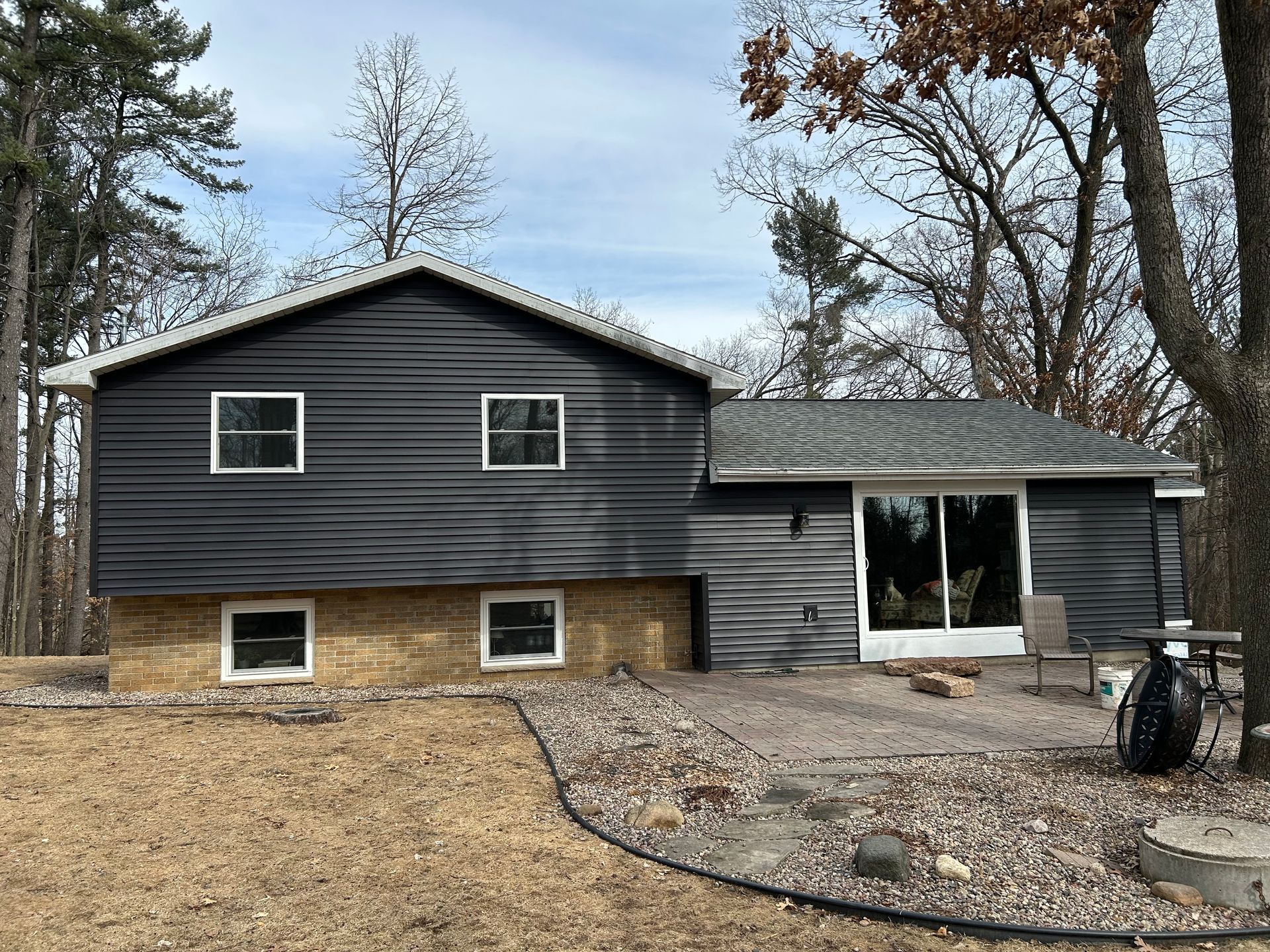 Dark gray sided house with a stone base, windows, and a sliding glass door.
