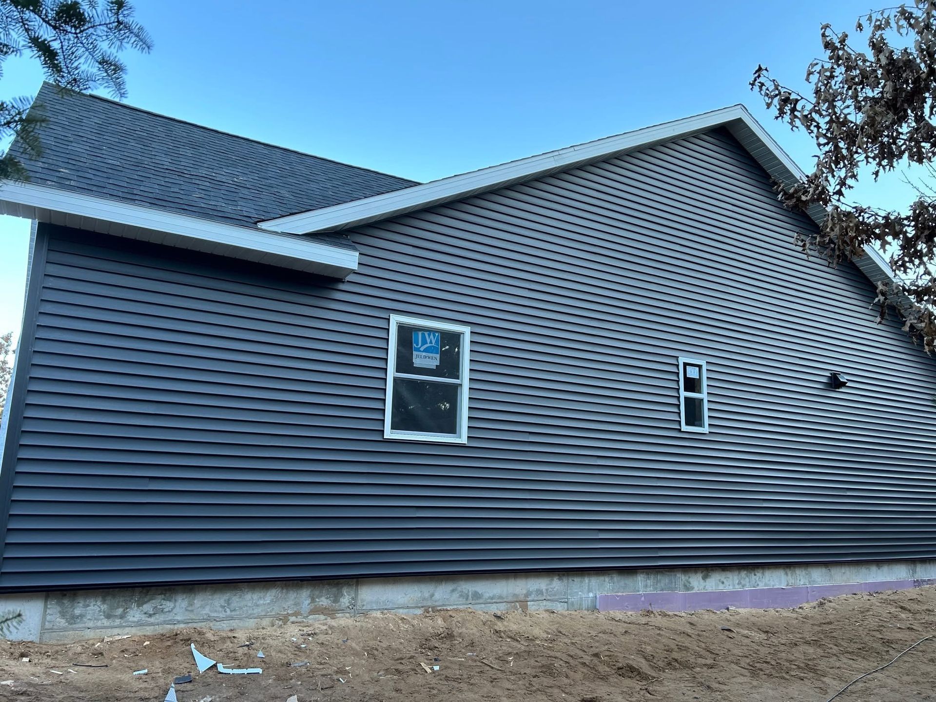 Dark gray-sided house with white trim under a blue sky; windows are installed, still under construction.