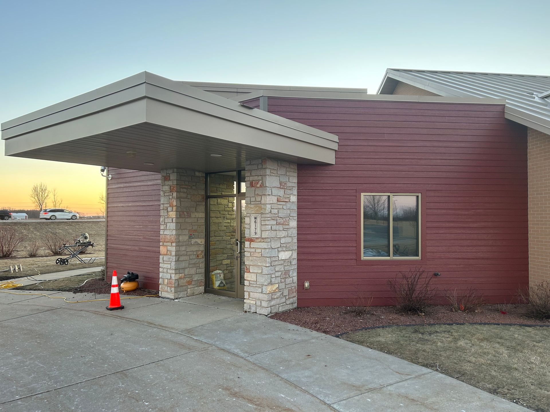 Building exterior with stone and maroon siding, covered entry, and orange cone.
