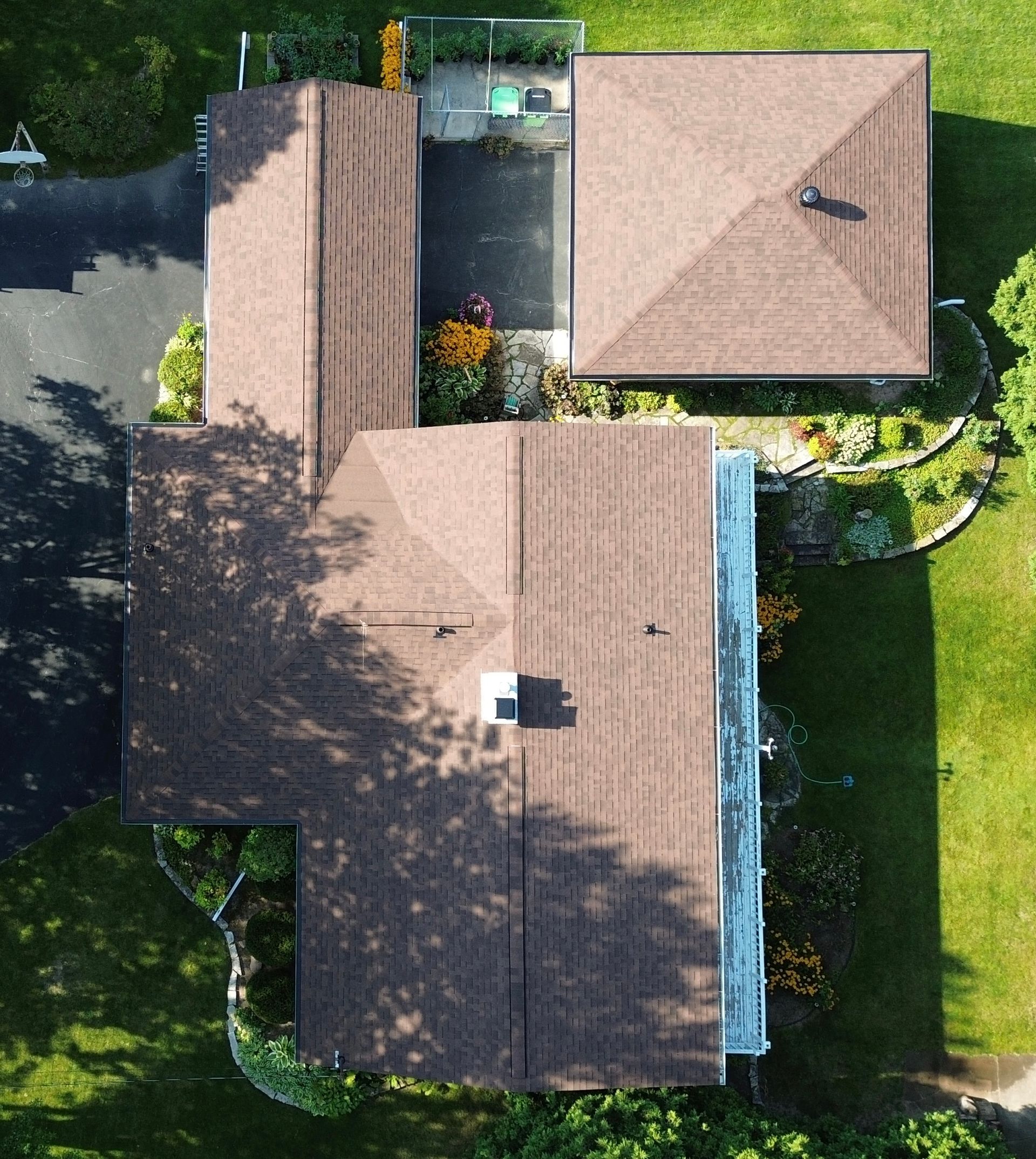 Overhead view of a house with brown roofs, a black driveway, and green yard with flower beds.