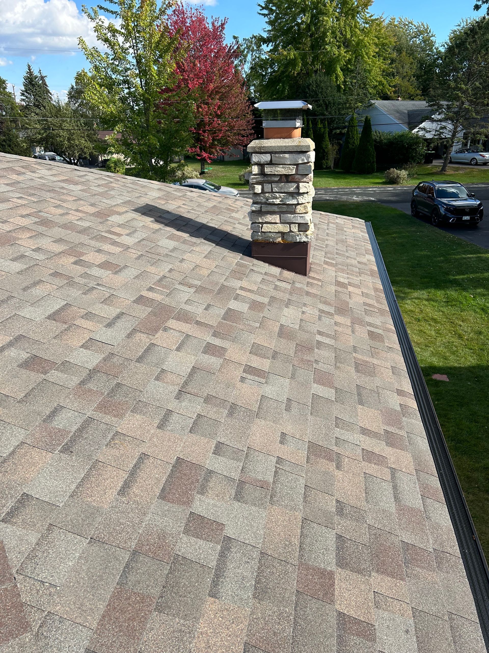 A roof with multi-colored shingles, a stone chimney, and a green lawn in the background.