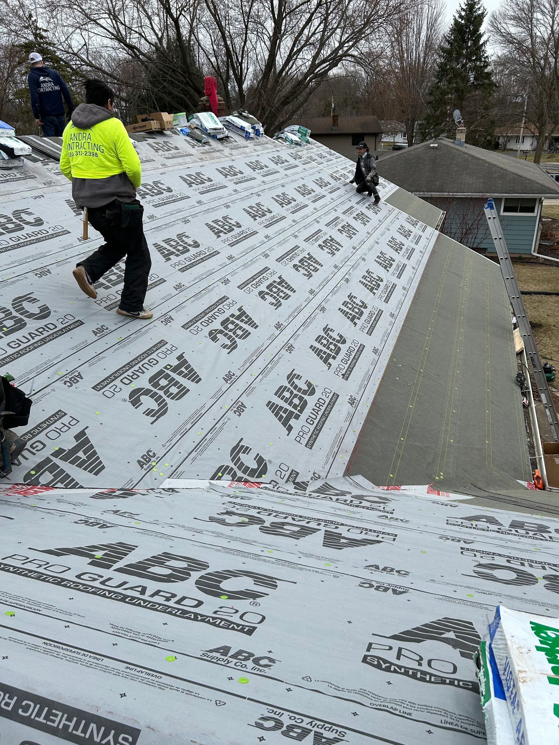 Construction workers laying synthetic roof underlayment on a house roof. One worker walks towards the camera.