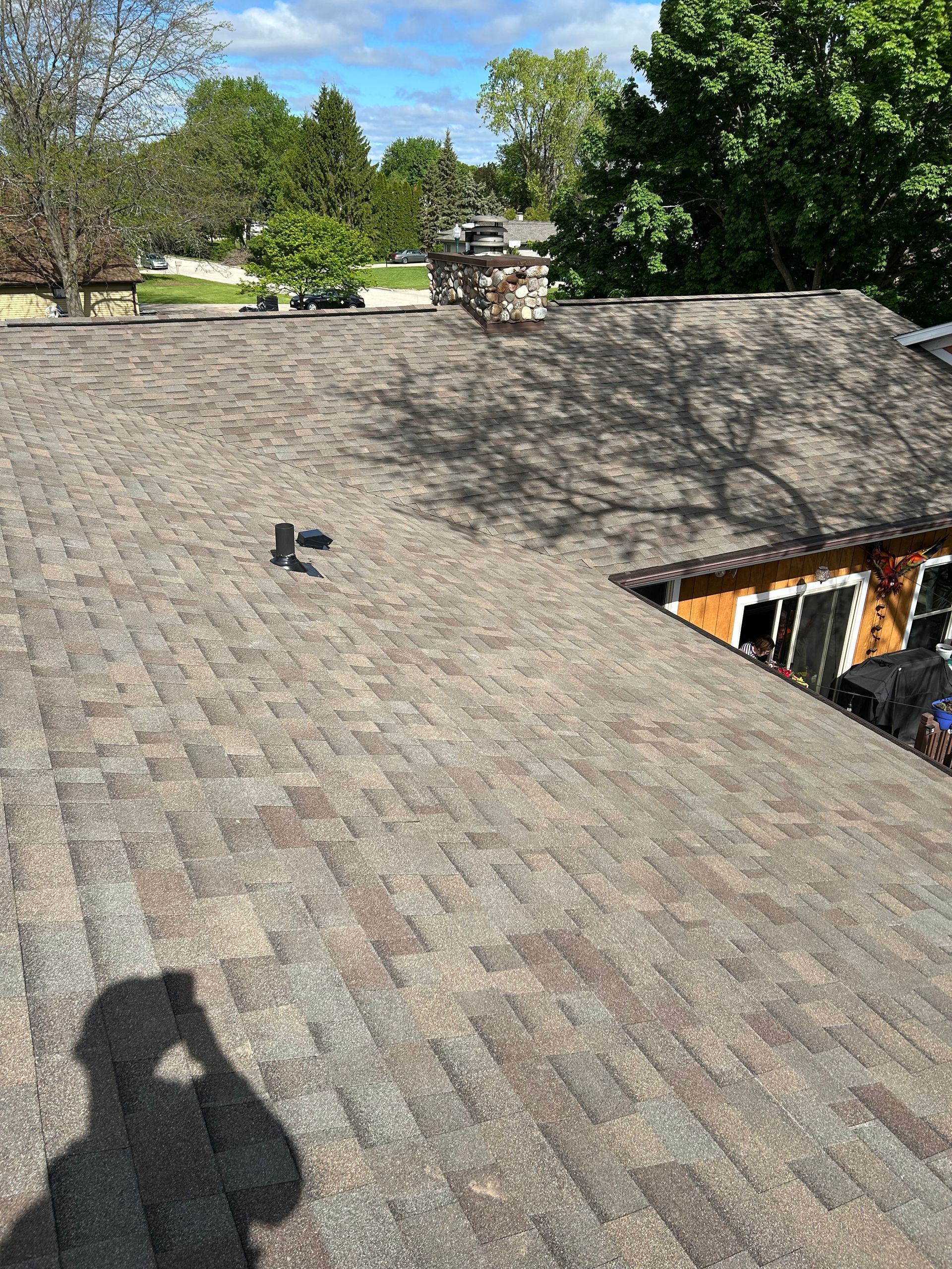 Brown shingled roof with chimney, vent pipe, and shadow of person holding a camera.