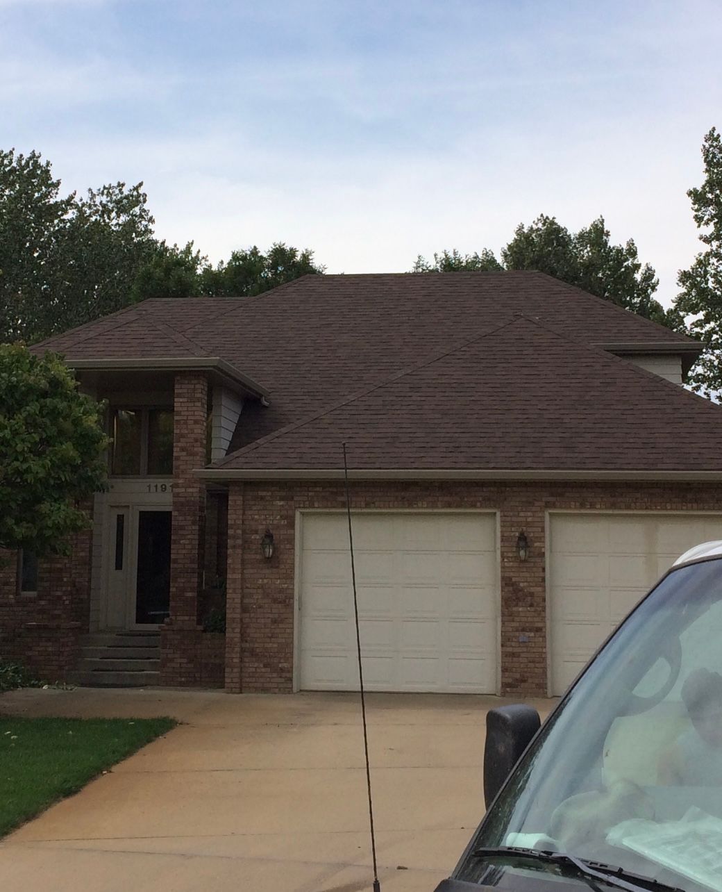 House with brown roof, brick and beige siding, two-car garage, and paved driveway. Overcast sky.