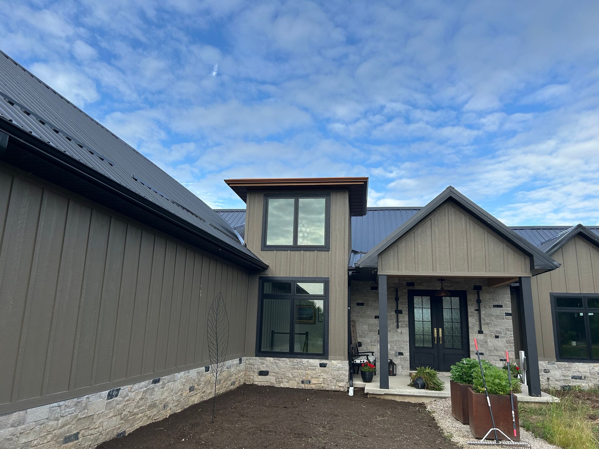 Modern home exterior with gray siding, black trim, and stone accents under a blue sky.