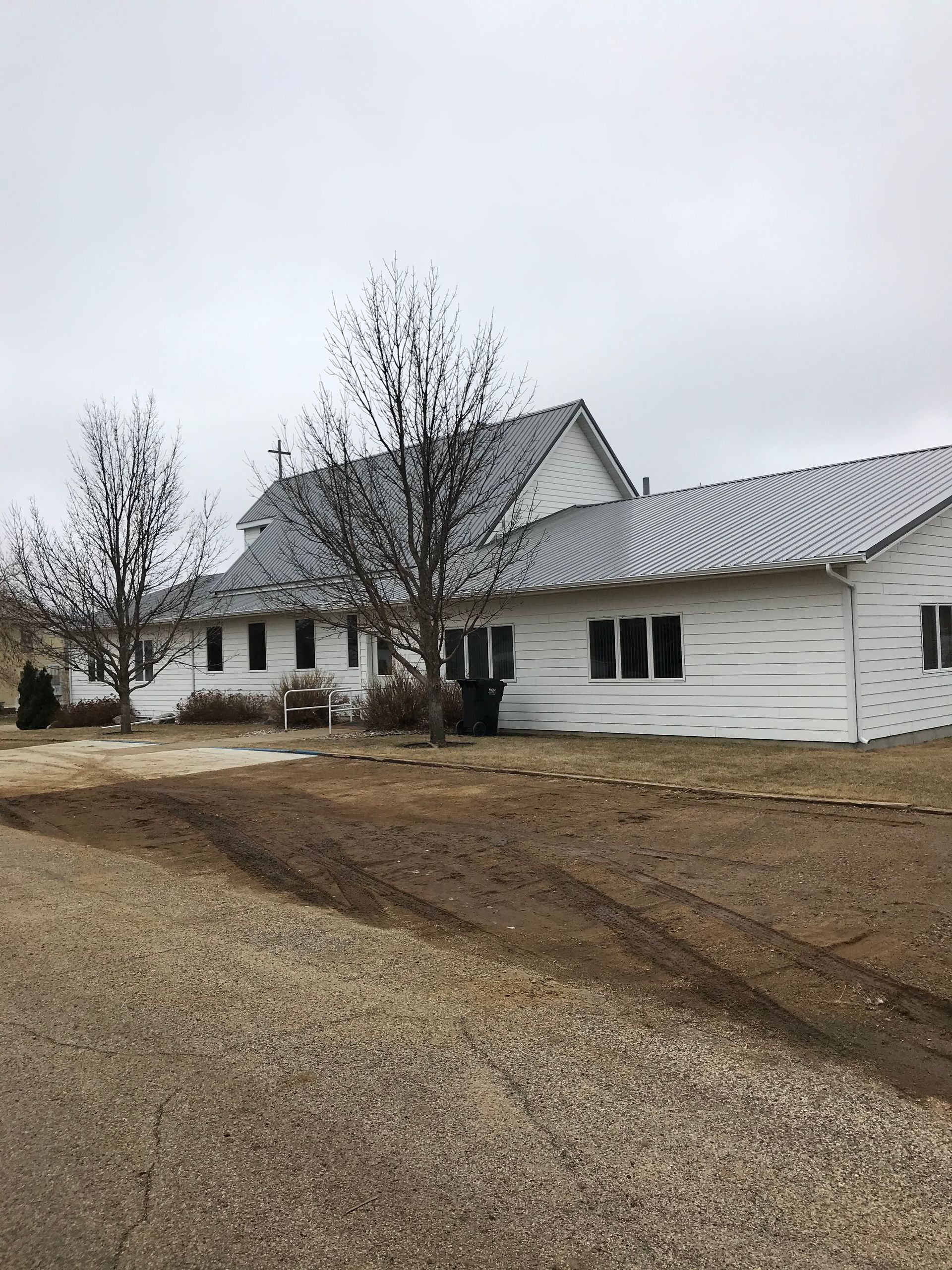 White farmhouse with bare trees on a cloudy day. Gravel driveway in foreground.
