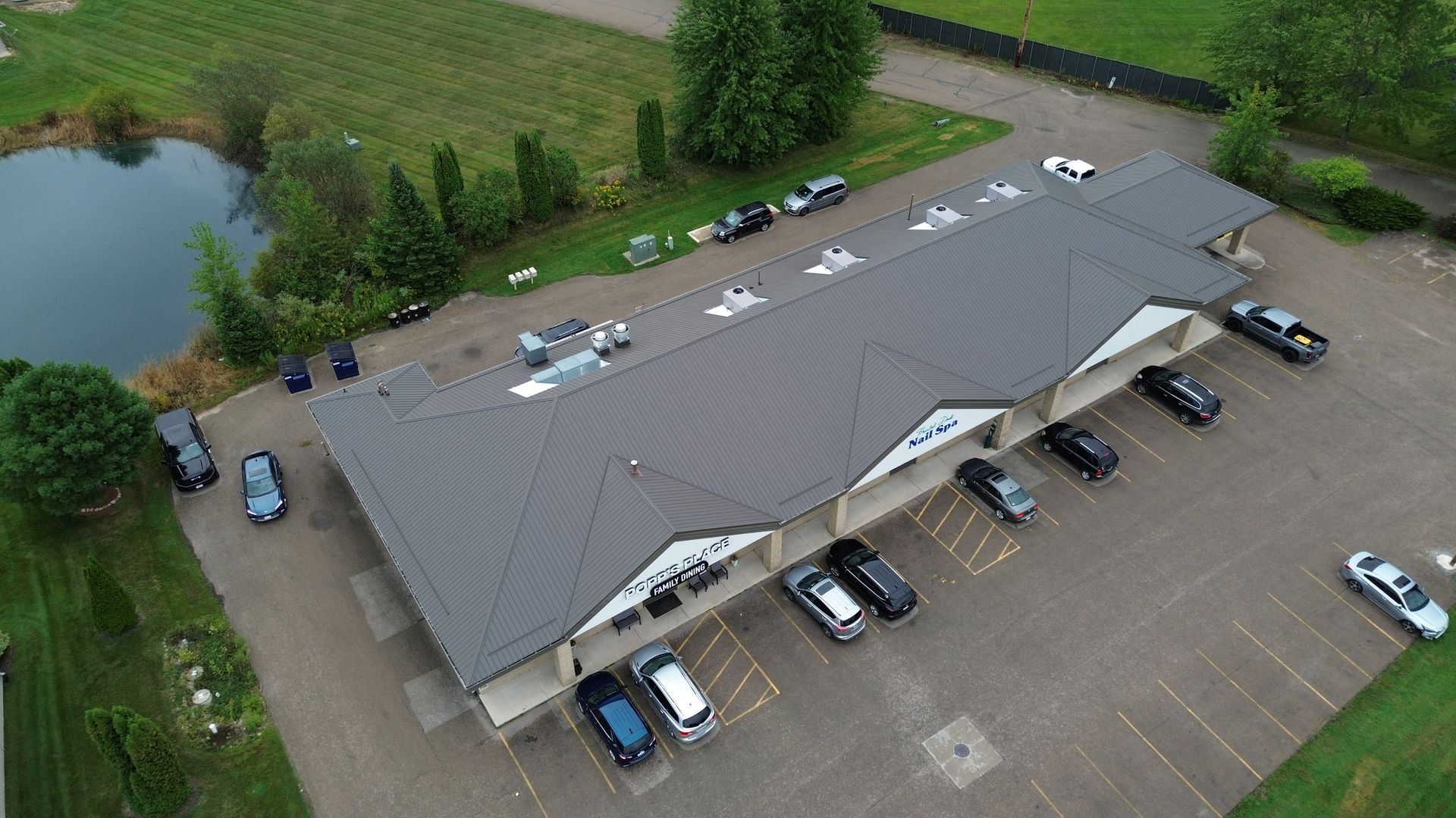Aerial view of a gray-roofed commercial building with parked cars