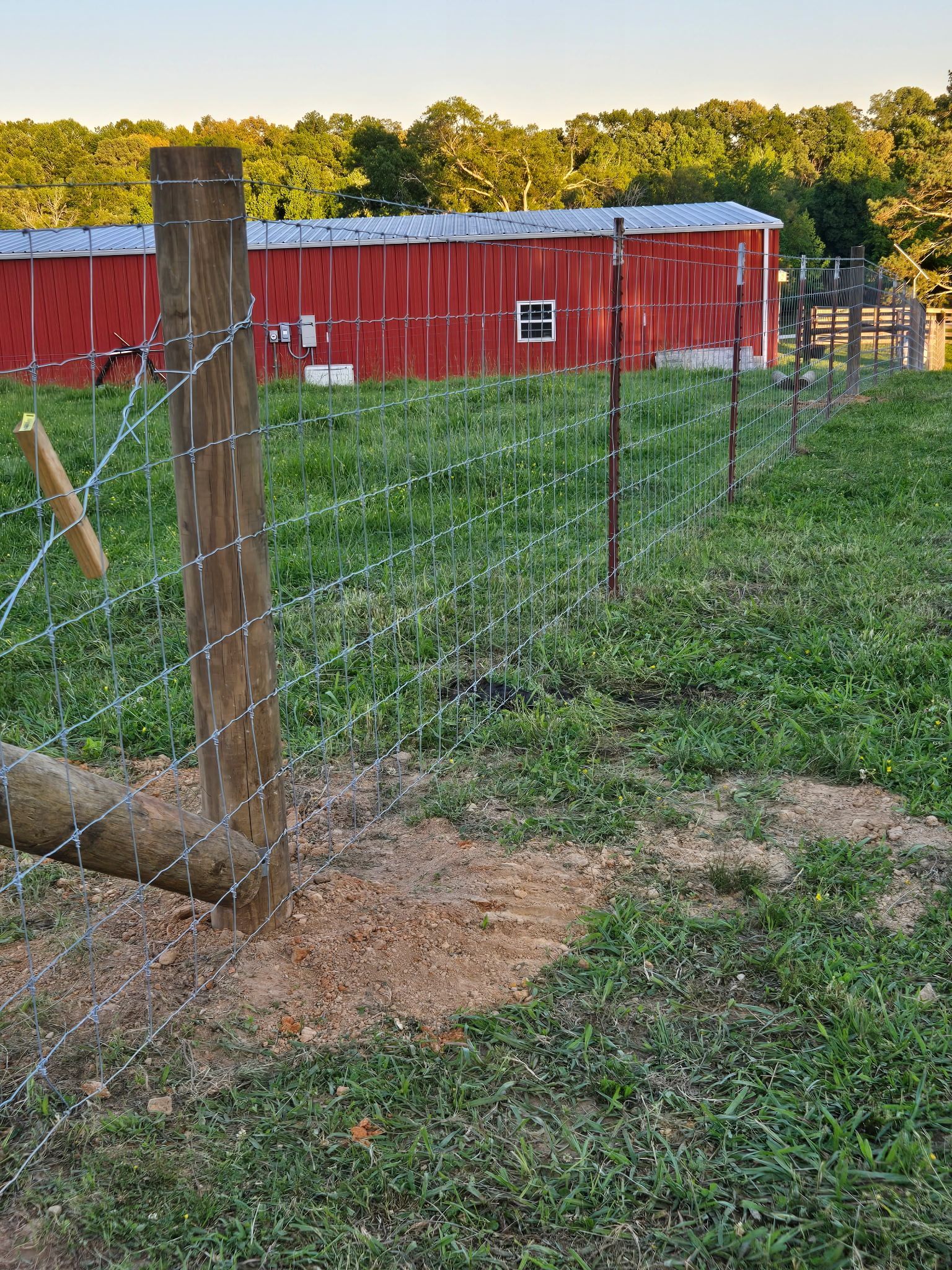 Wooden fence in front of a red barn, built on grassy land with trees in the background.