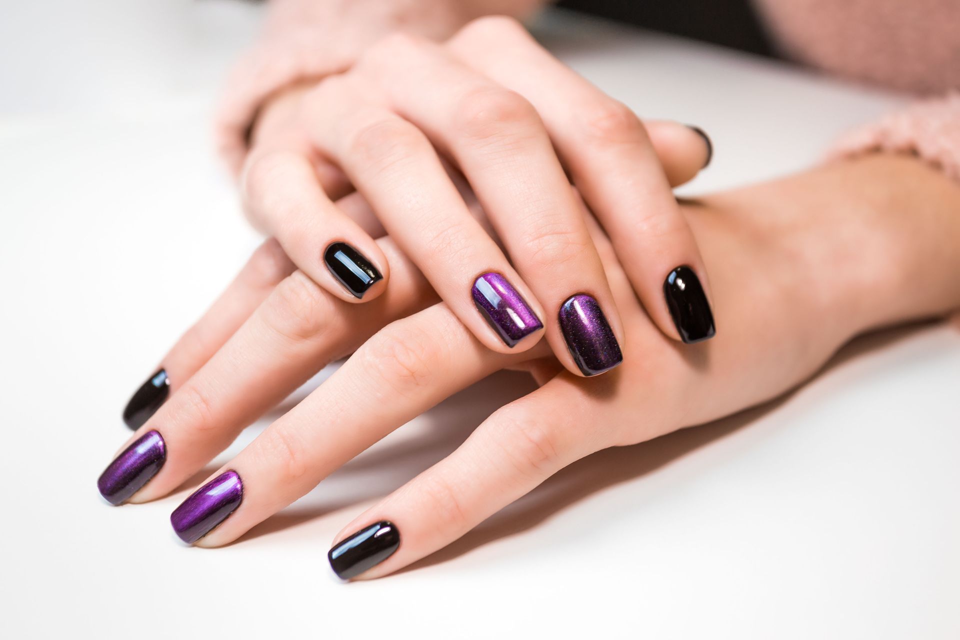 A close up of a woman 's hands with purple and black nails.