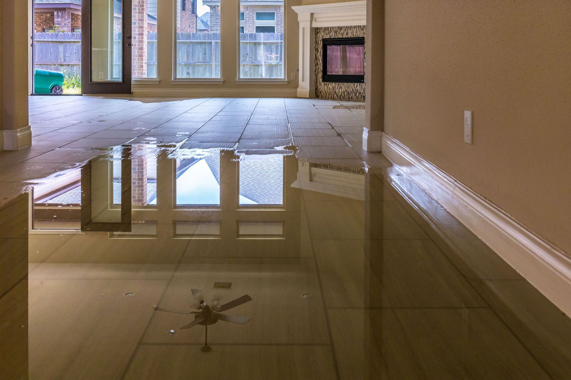 Flooded interior of a home; water covers tile floor reflecting windows and ceiling fan.