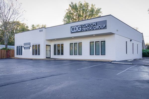 Exterior view of the Clayton Dental Group building, a white one-story dental office with large windows and a parking lot.