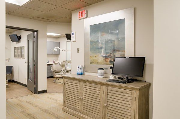 Hallway in a dental office; wooden cabinet with a computer; artwork on the wall, open doorway to an exam room.