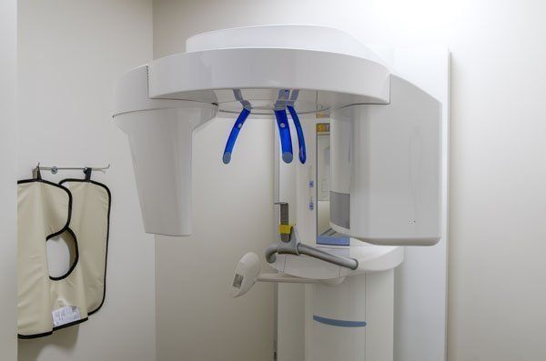 Panoramic dental X-ray machine in a dentist's office, with a lead apron hanging on the wall.
