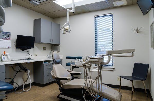 Dental office interior: dentist chair, equipment, cabinets, desk, window with blinds.